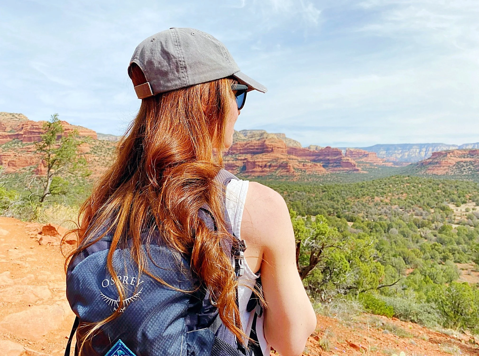 Lucia wearing a hat and backpack, looking out over a valley in Sedona, Arizona