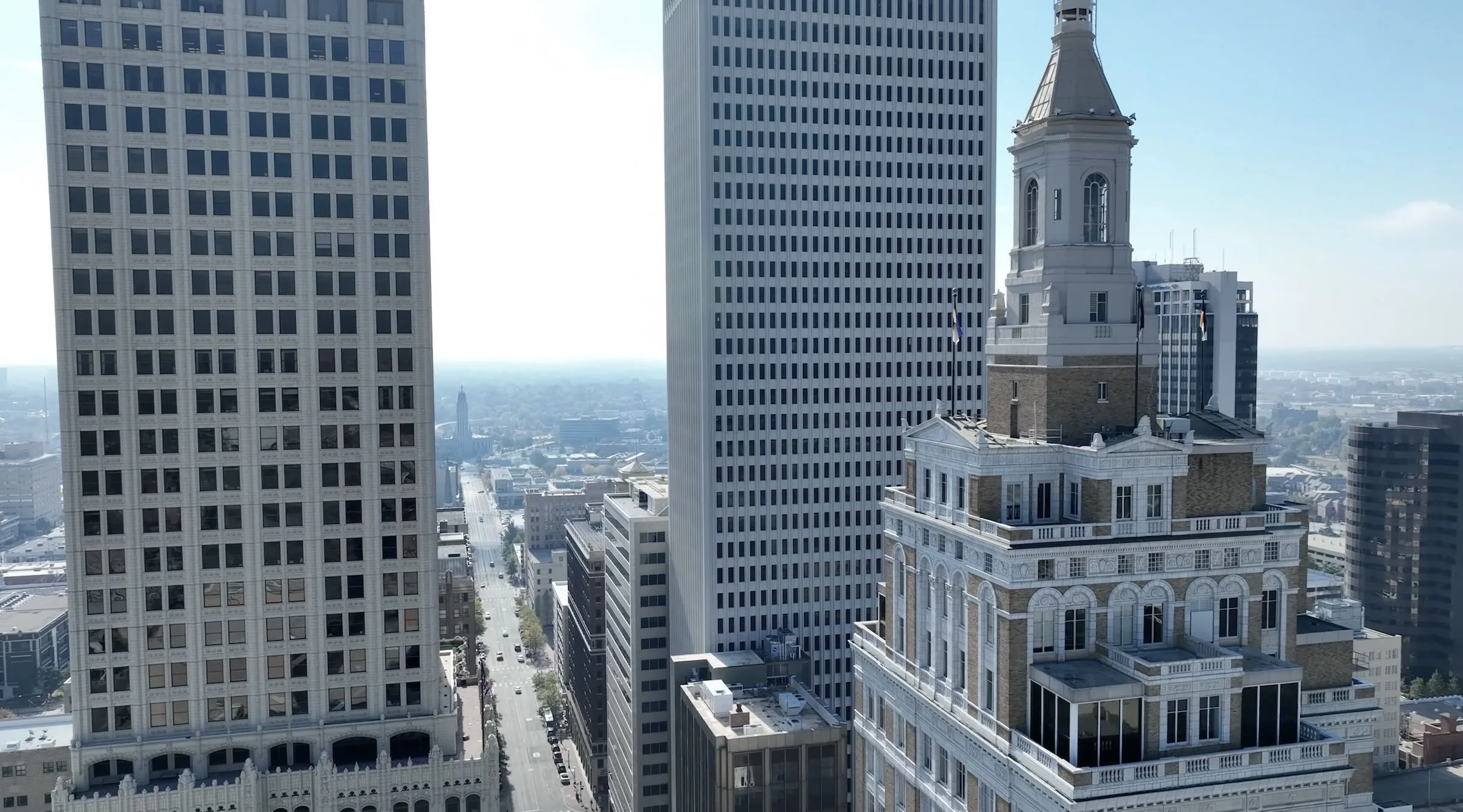 Cityscape featuring tall skyscrapers, including a historic building with a clock tower in the foreground and modern high-rise buildings in the background, under a clear blue sky.