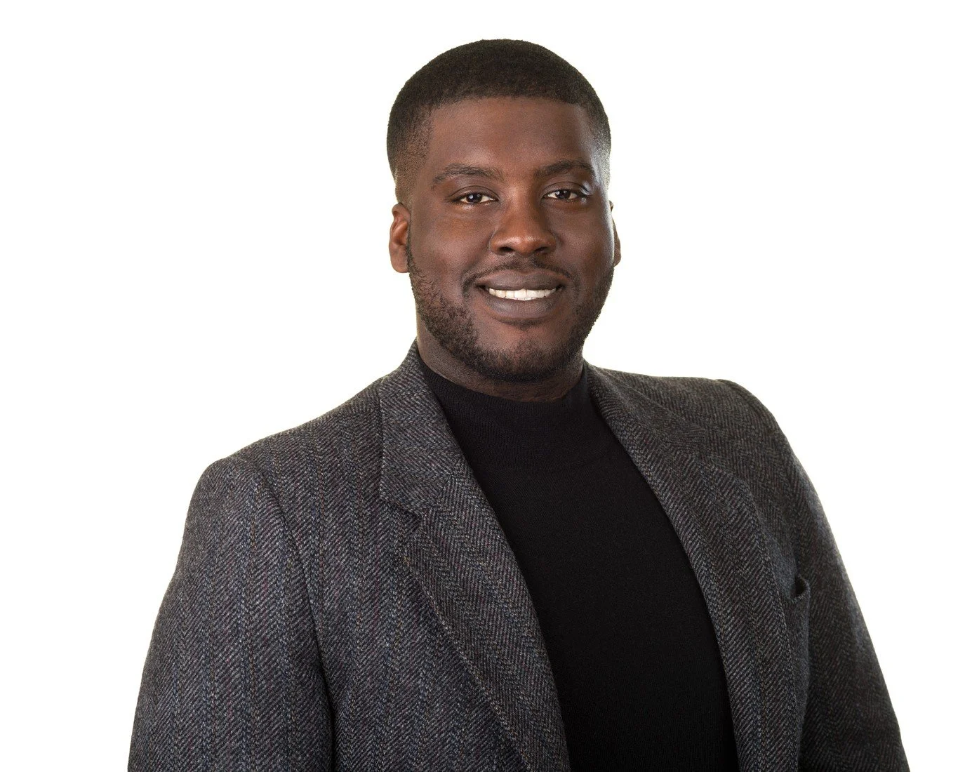 Sheldon Mellis, Director od Strategic Partnerships and Engagement, wearing a grey jacket and black shirt in front of a white background.
