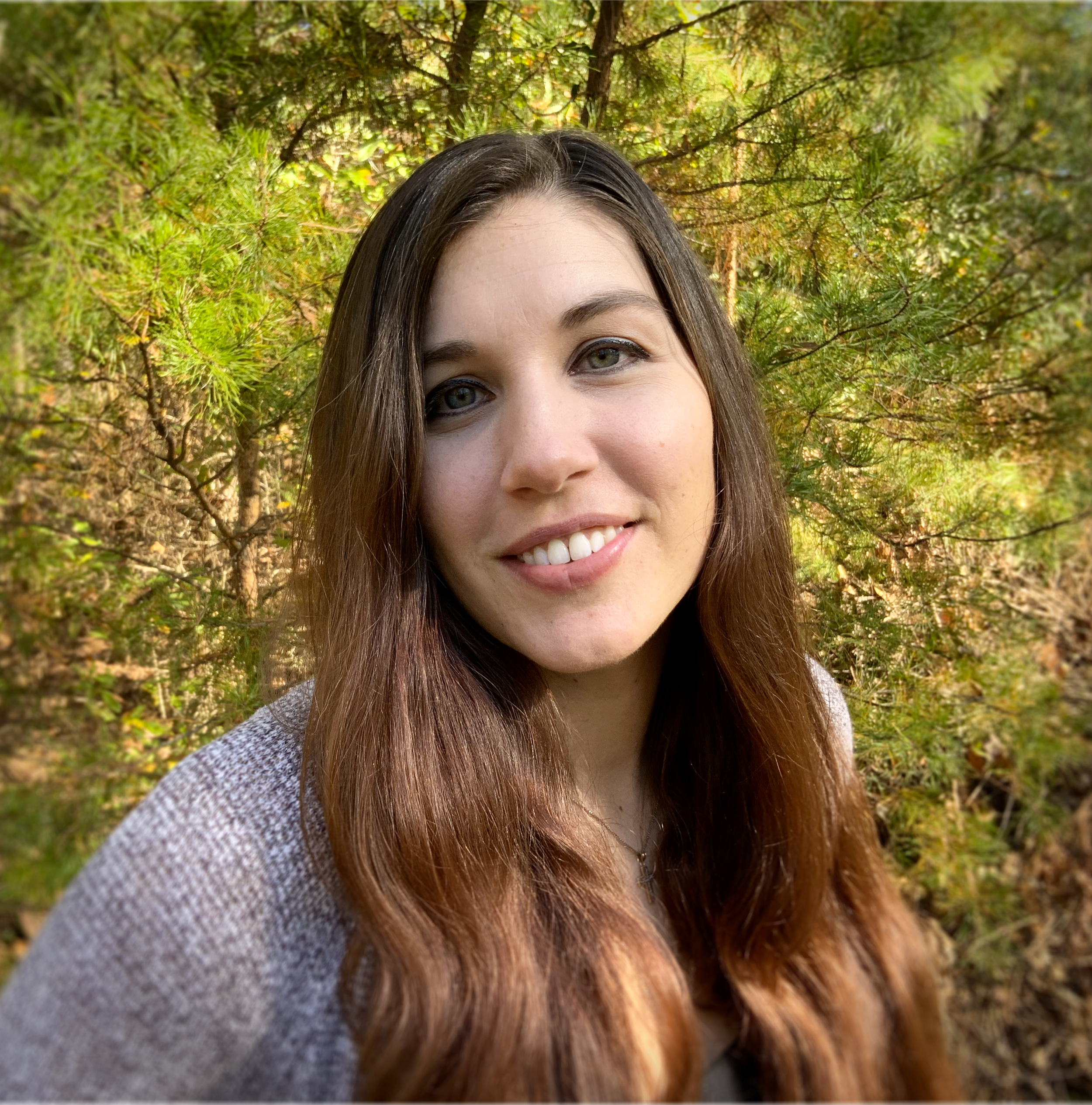 Person smiling outdoors with green foliage background.