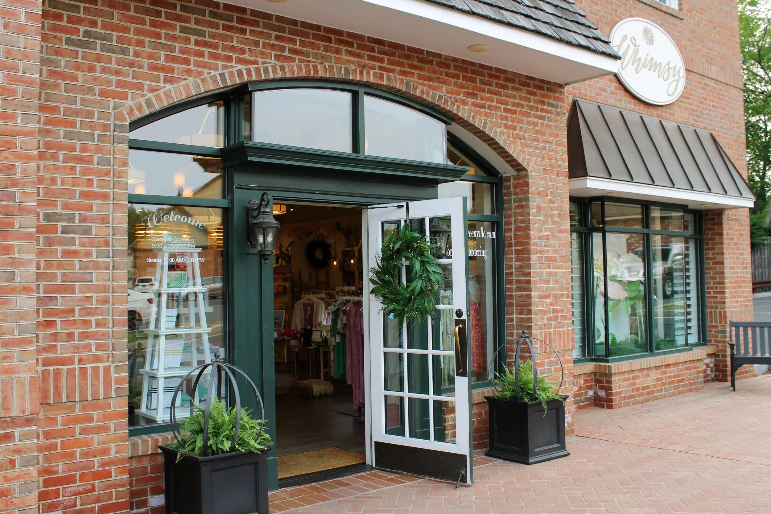 Exterior view of Whimsy gift shop in Greenville, Delaware featuring open door, storefront windows, and inviting brick walkway entrance.
