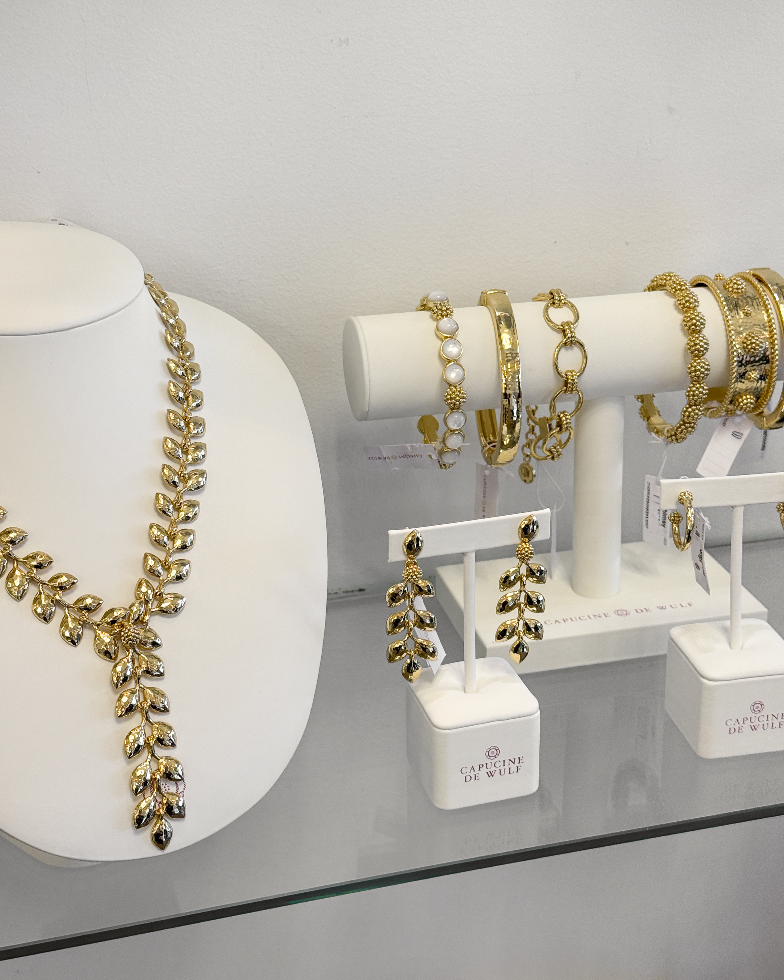 Gold statement necklace, matching drop earrings and bracelets displayed on white jewelry stands.