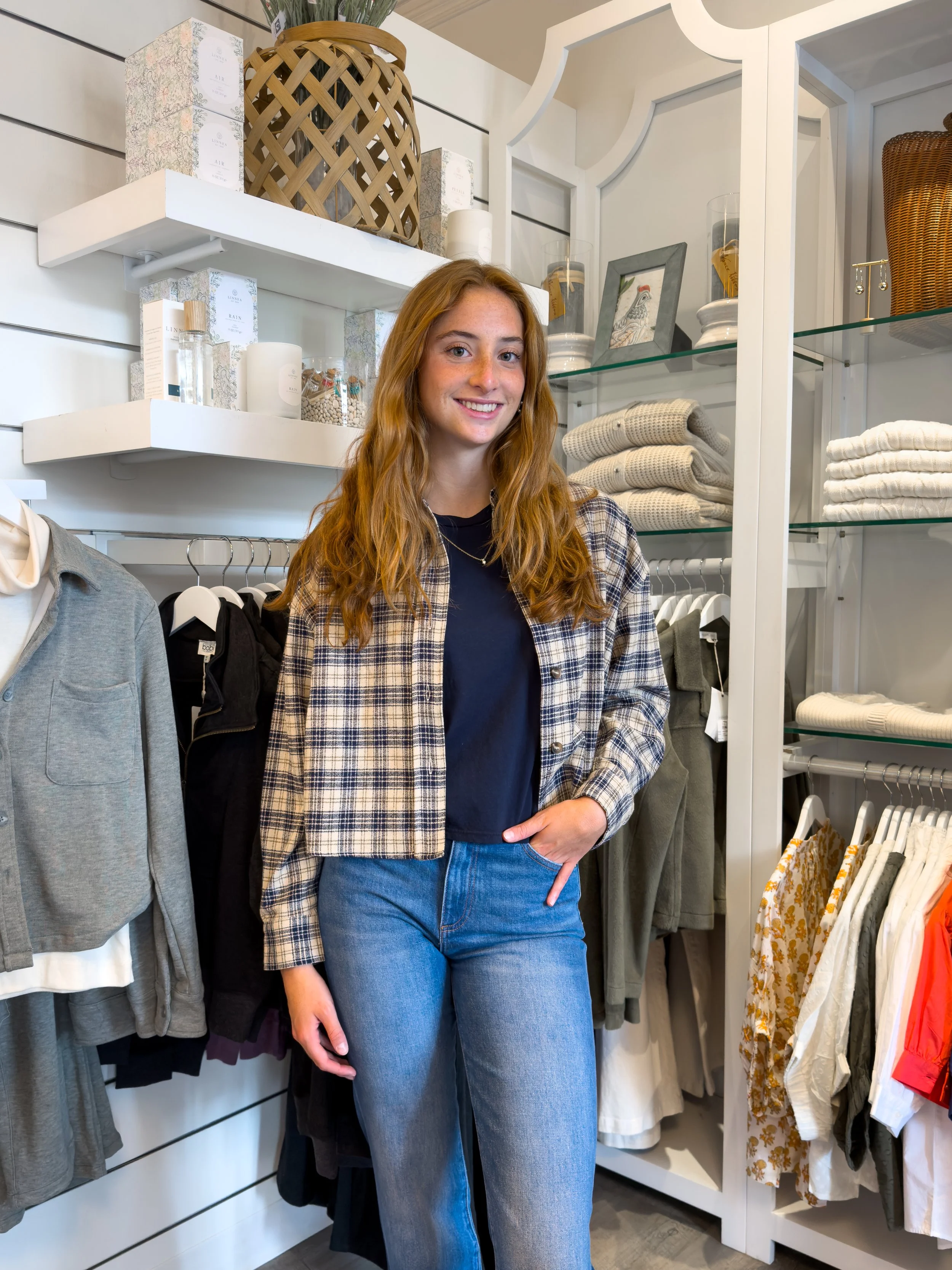 Young woman wearing a navy top, blue jeans and a cream-and-navy plaid jacket inside Whimsy boutique in Delaware.