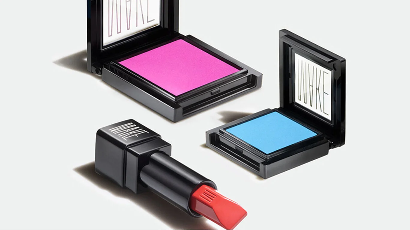 Two makeup compacts with mirror lids, one containing pink blush and the other blue eyeshadow, and a tube of lipstick with red lipstick.