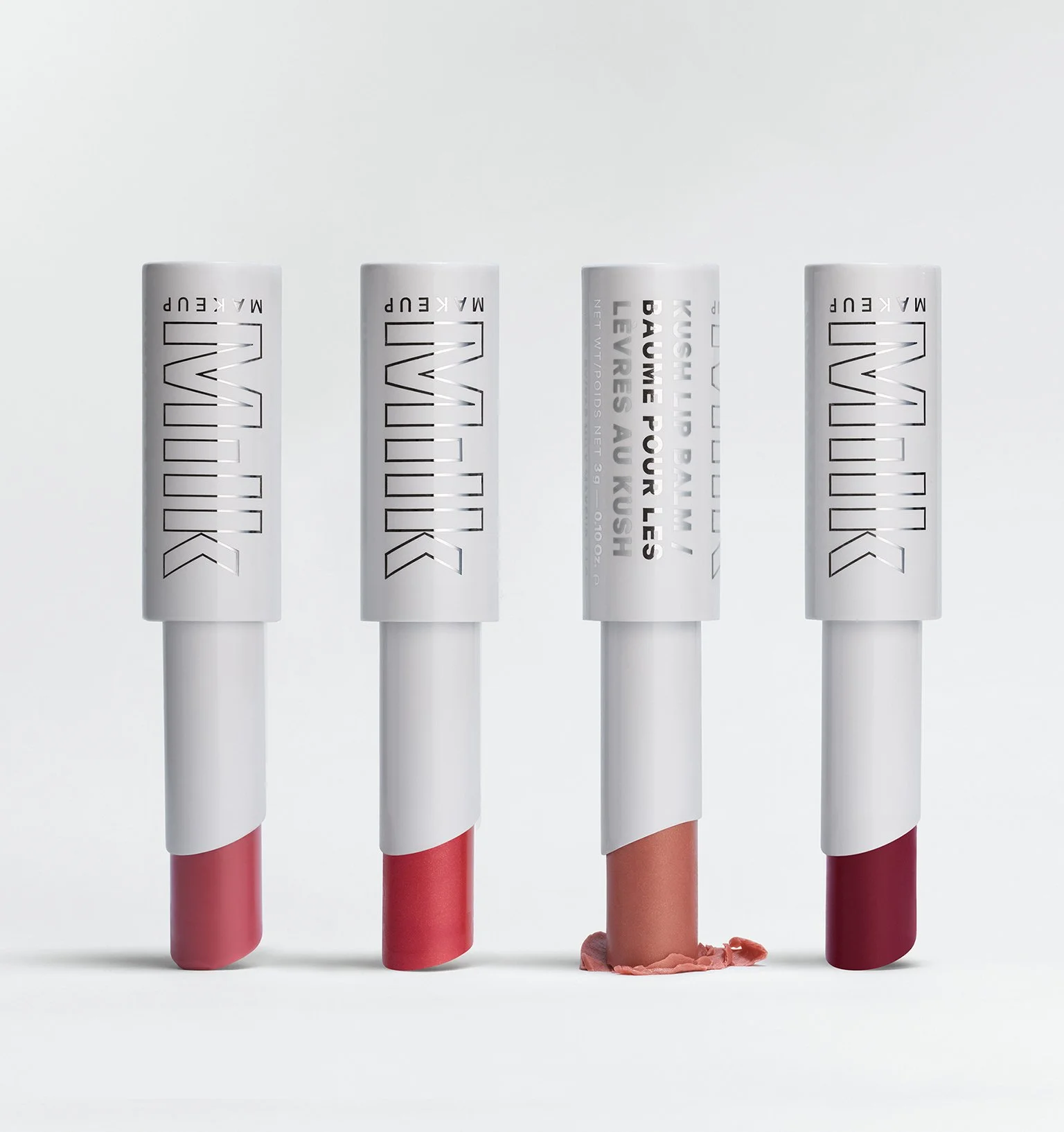 Four lipsticks with white caps and different shades of lipstick, one of which is melted and smeared.