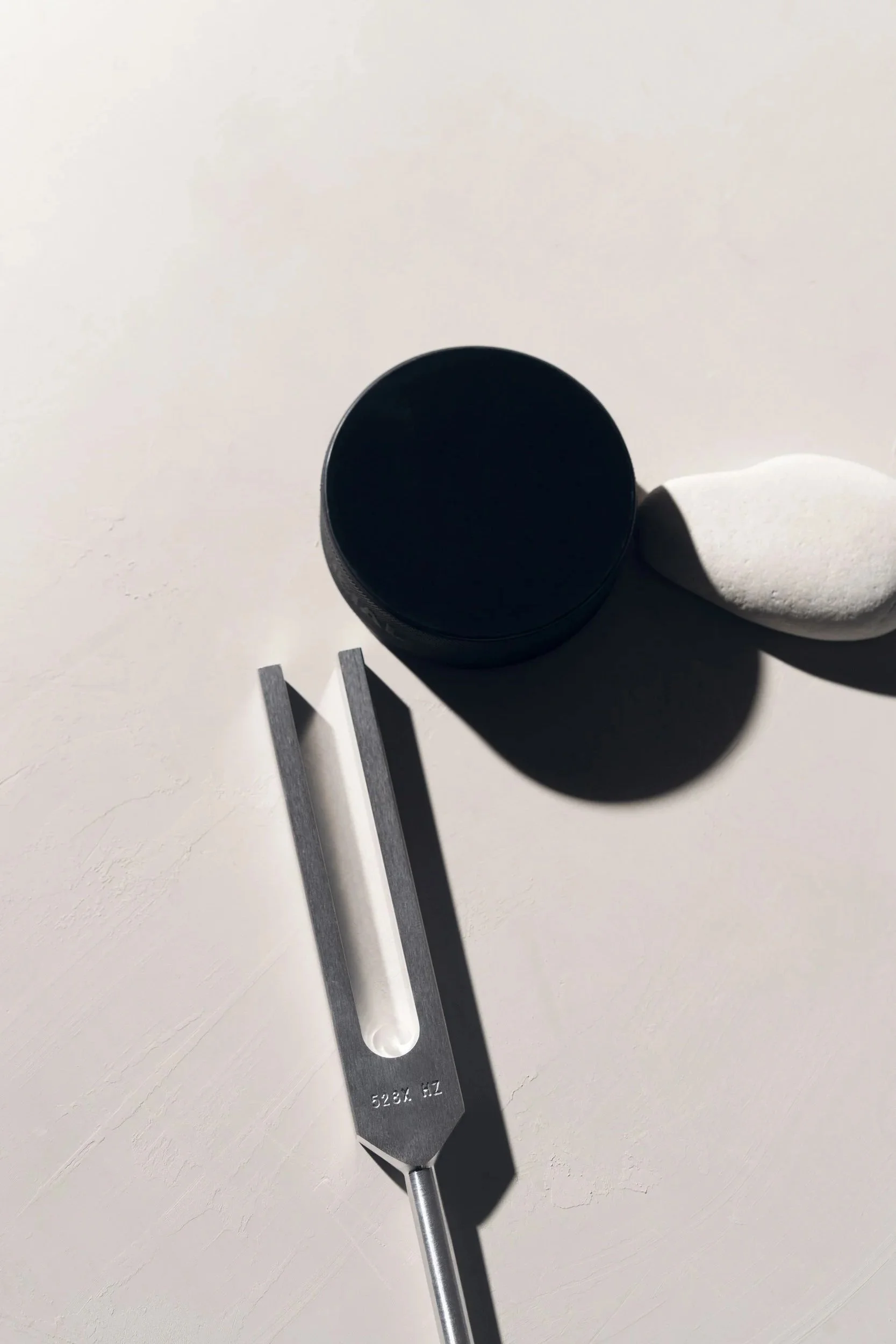 A Biofield Tuning fork and puck are on a white surface, with shadows cast by the objects.