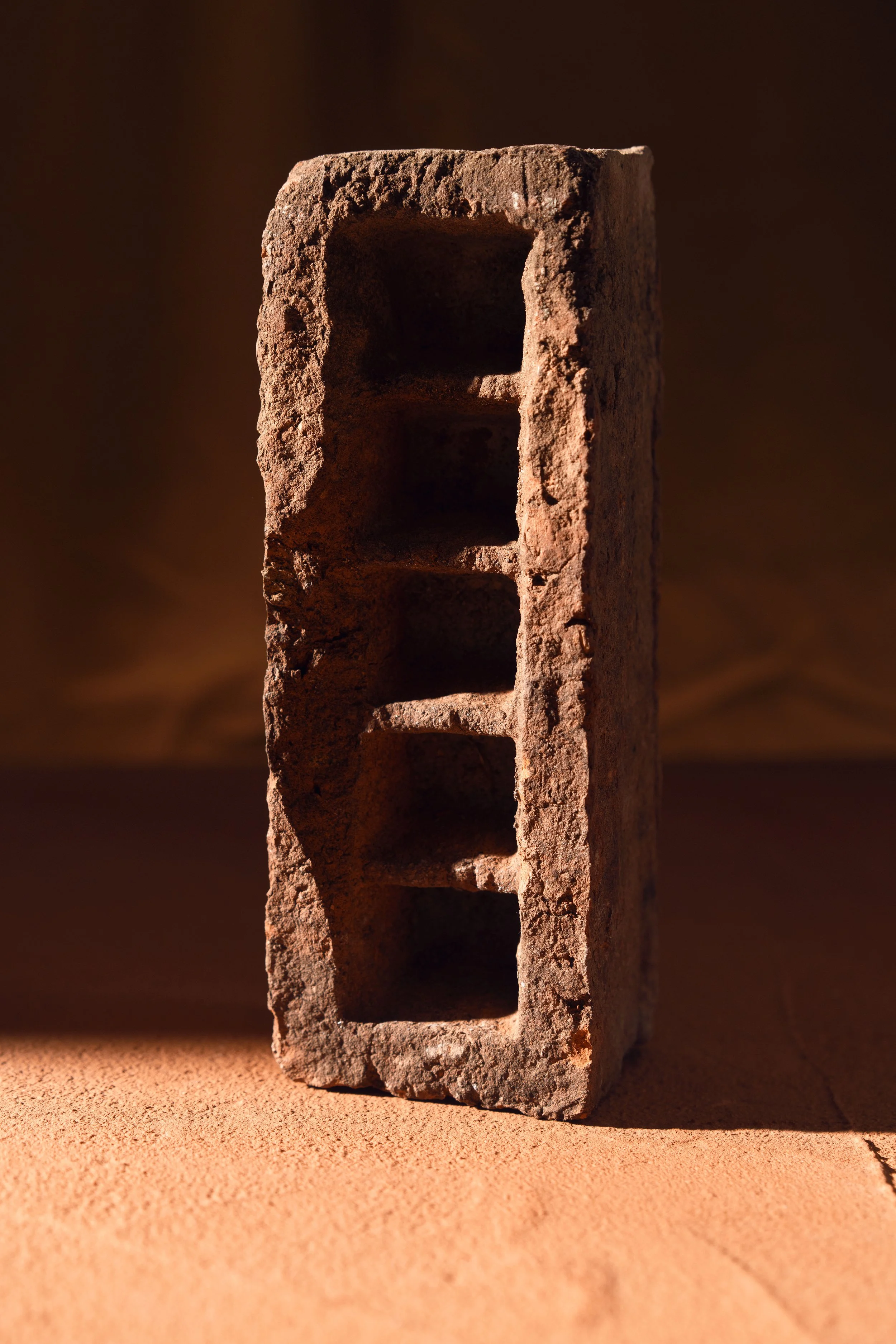 Close-up of a weathered red brick with four rectangular holes, set against a dark background with warm lighting.