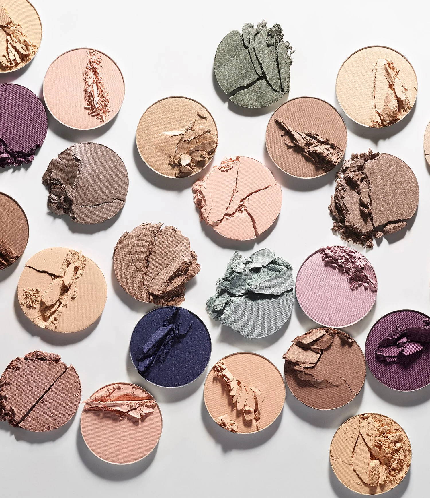 Various broken pieces of pressed powder eyeshadows in different shades arranged on a white background.