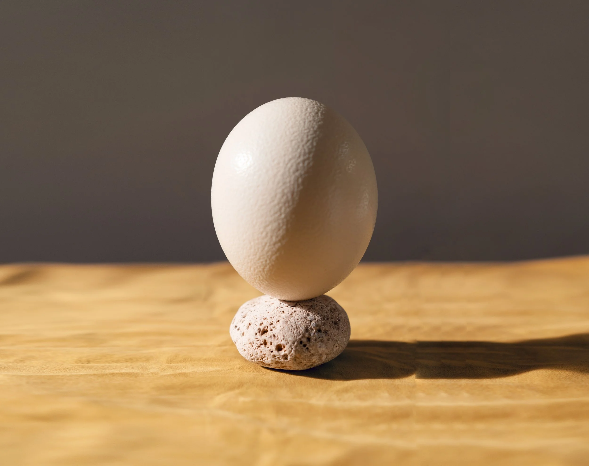 An egg balanced on a small rock on a wooden surface with soft lighting.