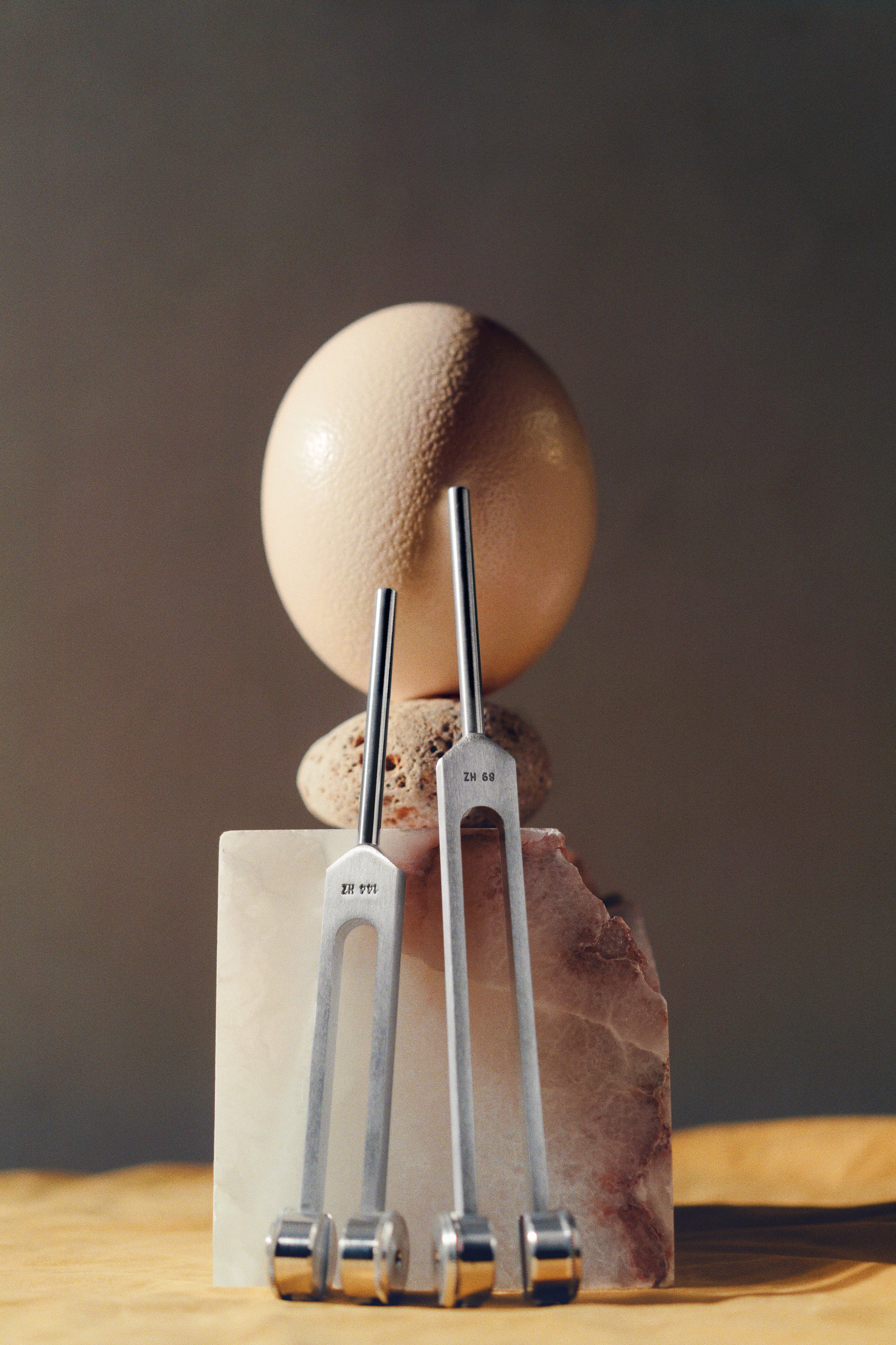 A marble serves as the base for a stack of rocks, with a large egg and two Biofield Tuning forks placed on the rocks, against a neutral background.