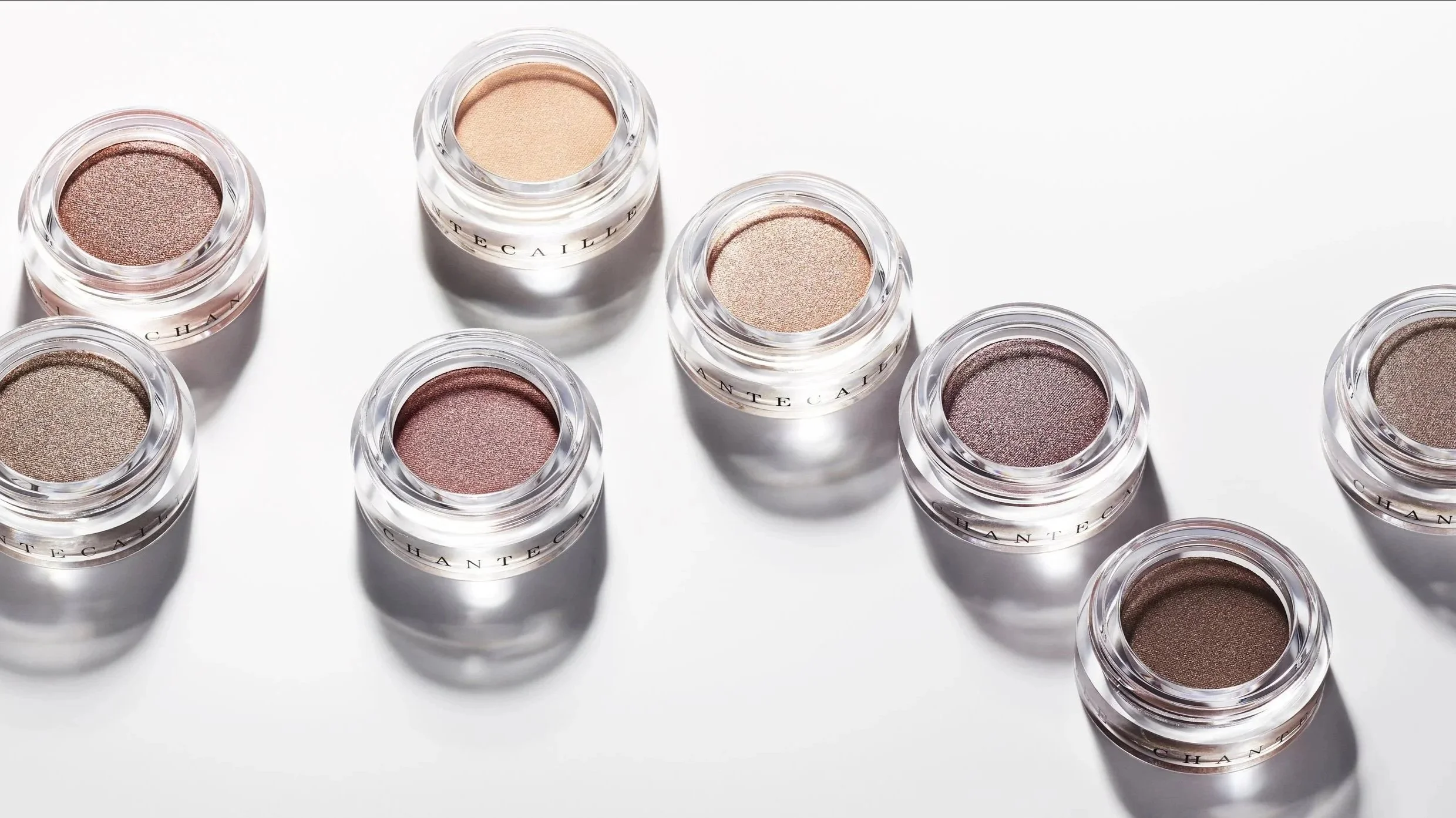 Nine small jars of neutral-toned eyeshadow arranged on a white surface.