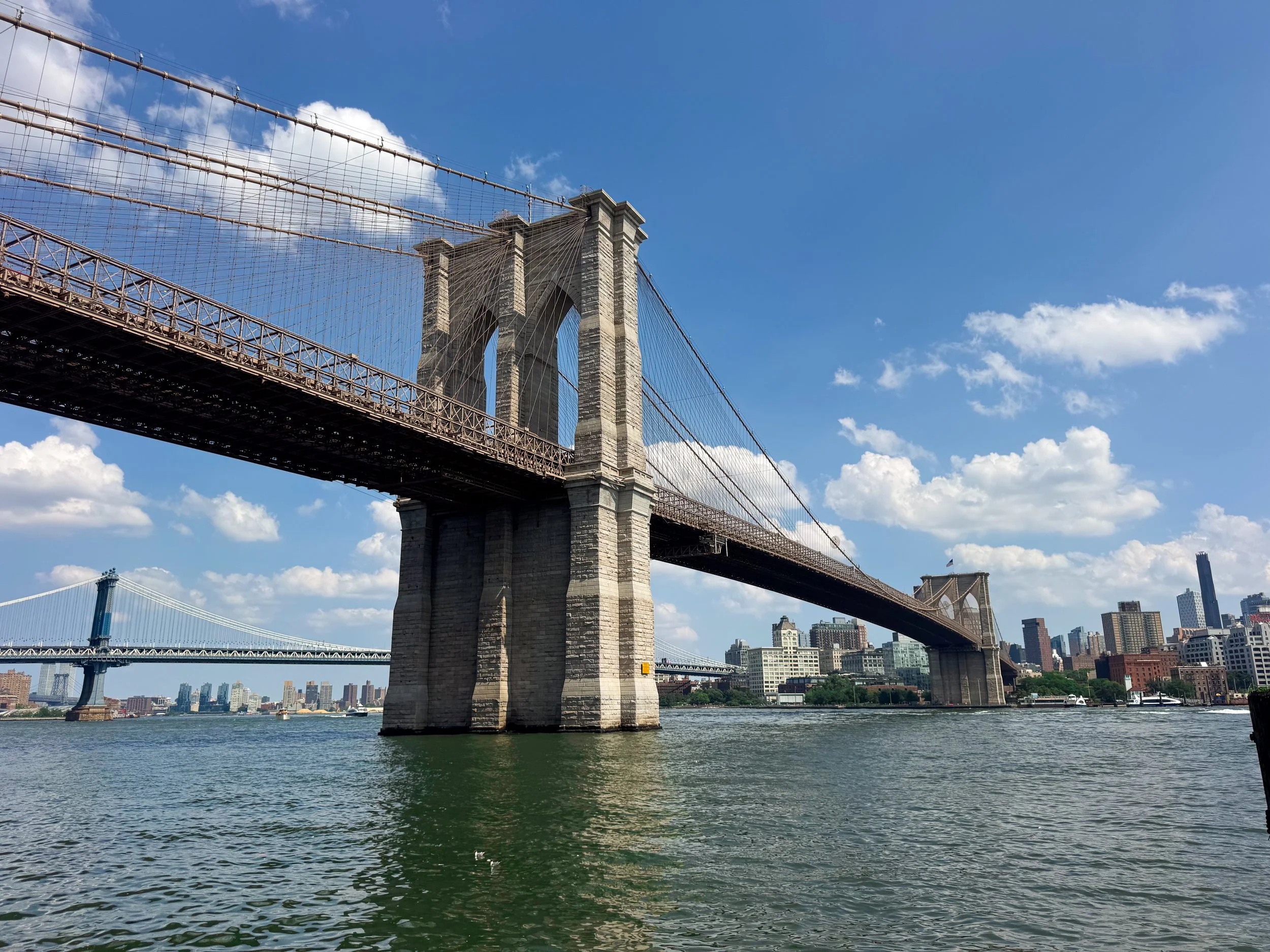 Stone towers and steel cables of the Brooklyn Bridge spanning the East River with the Manhattan Bridge and skyline behind