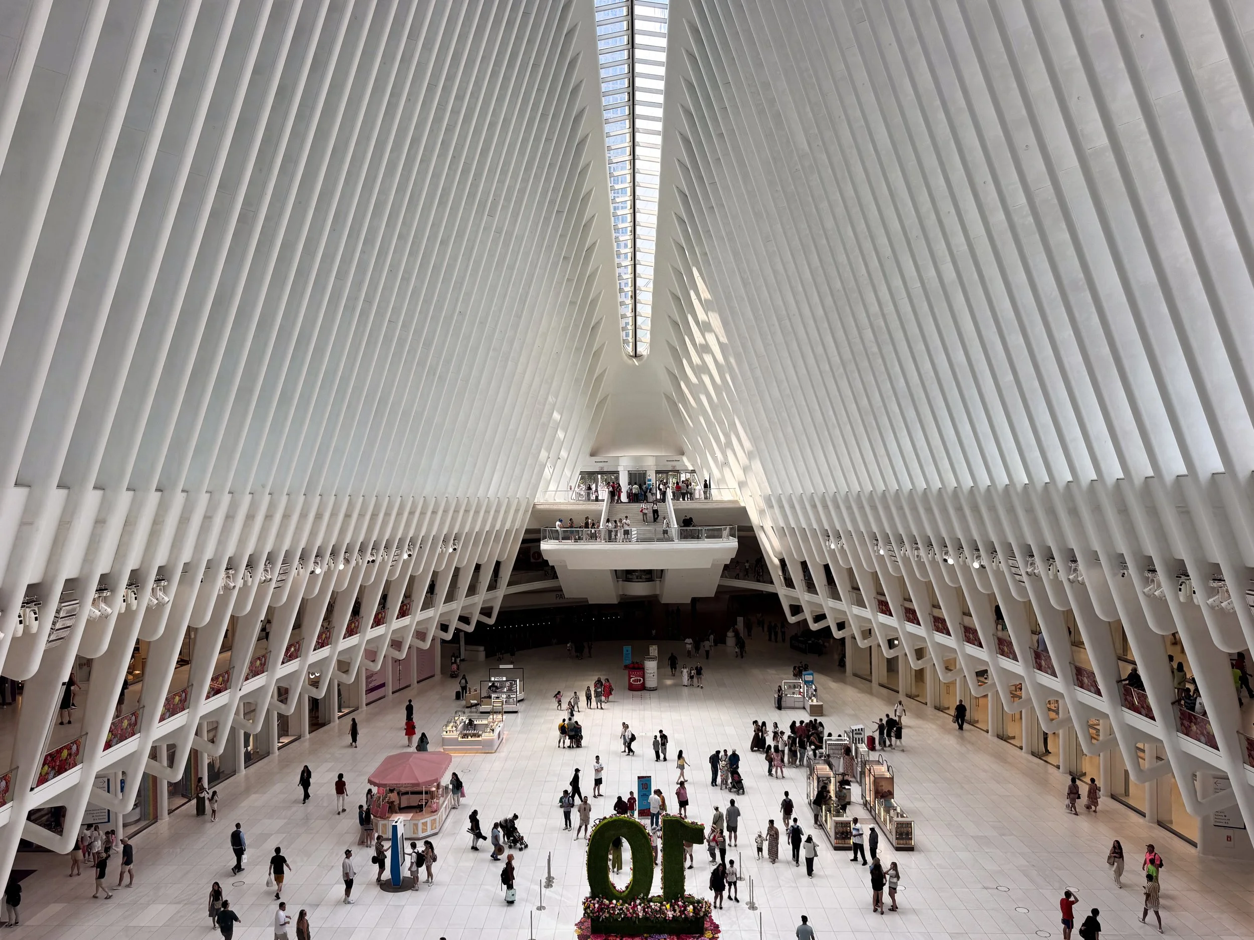 Soaring white ribbed interior of the Oculus transit hub with shoppers crossing the bright marble floor beneath a central skylight
