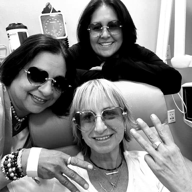 Three women wearing sunglasses in a hospital room, smiling and showing their rings, with medical equipment in the background.