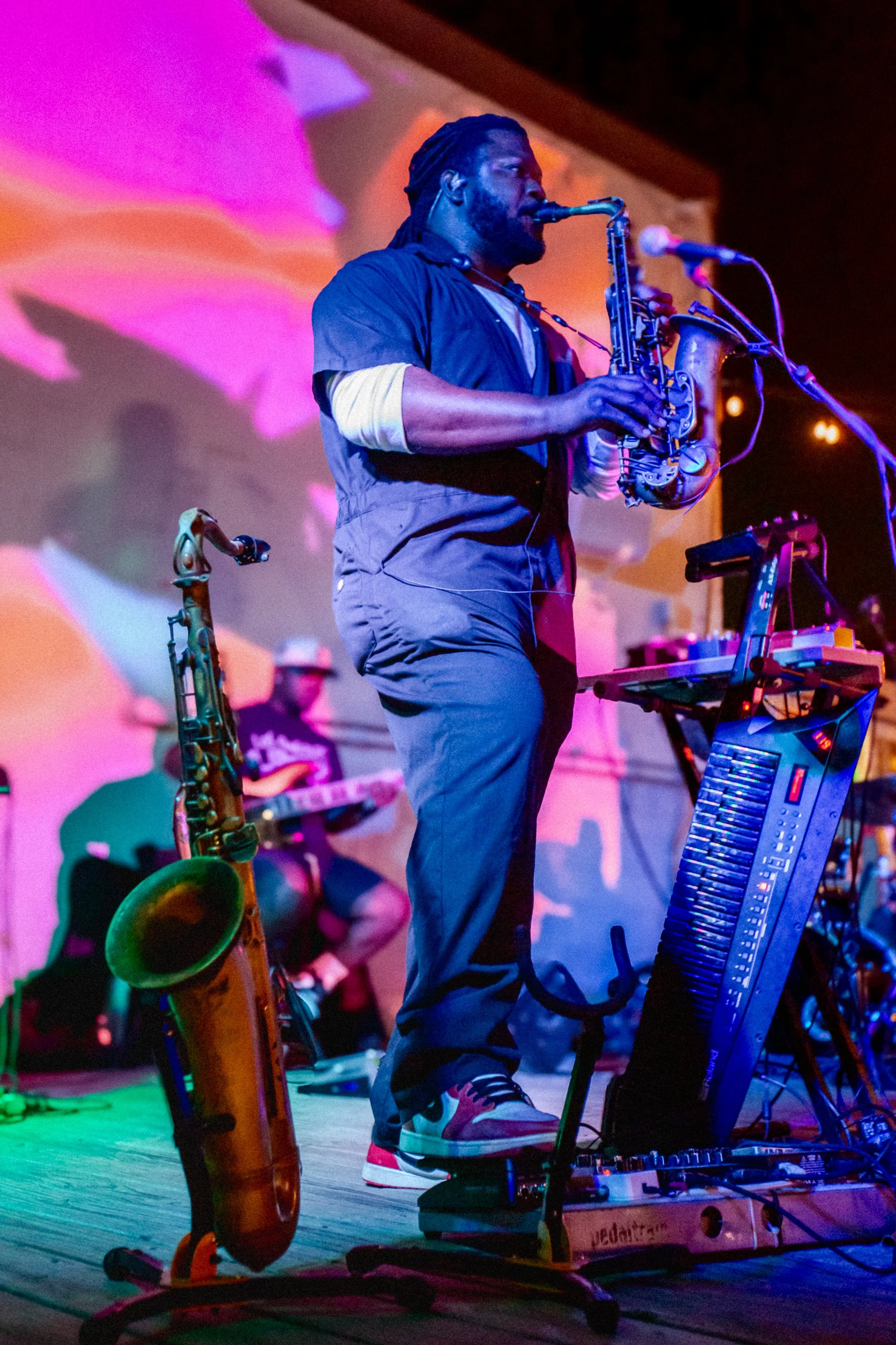 A man with long dreadlocks singing into a microphone, with colorful lights and a glowing background behind him.