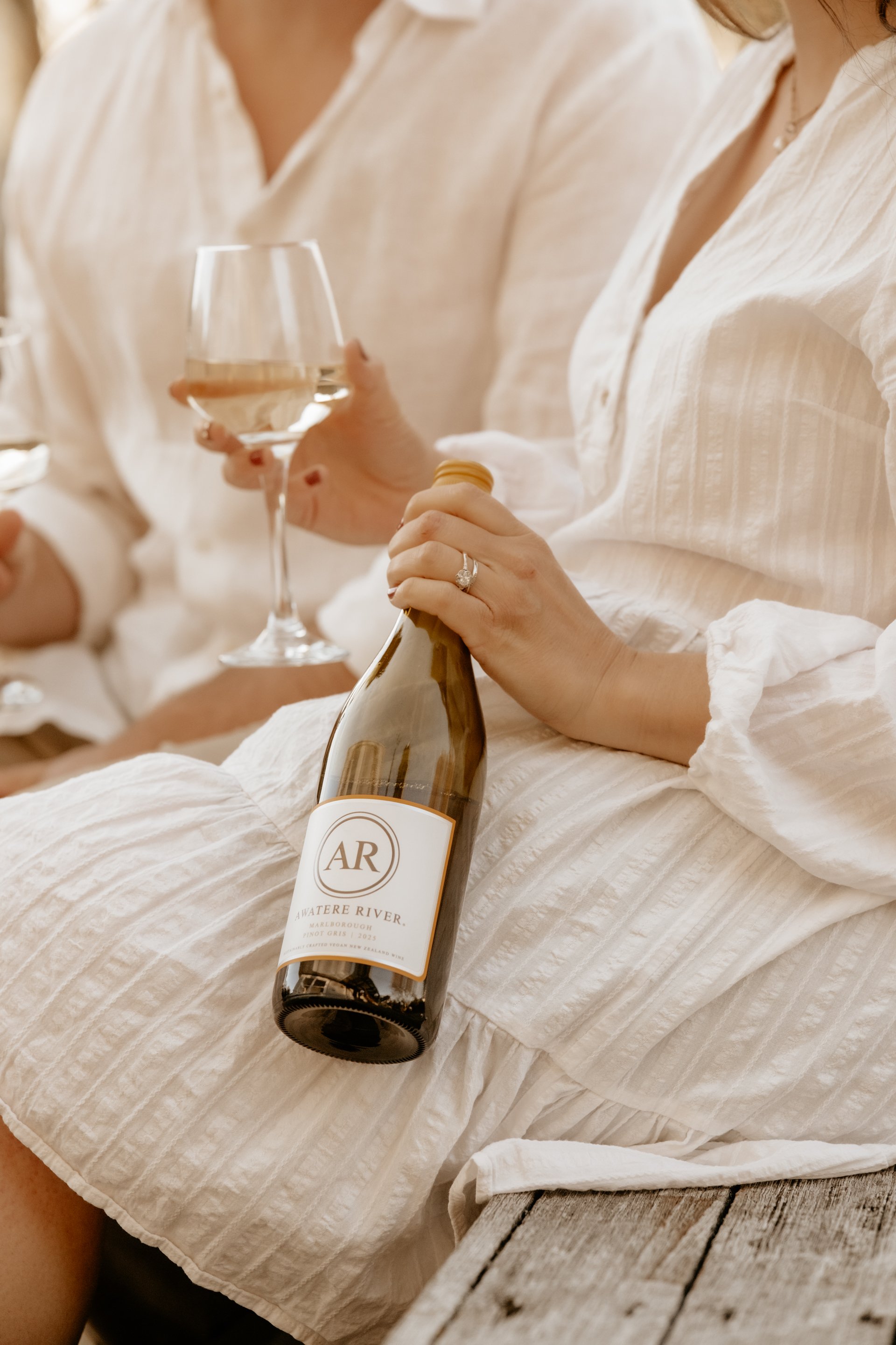 Person in a white dress holding a wine bottle labeled 'A Watere River' and a glass of white wine.