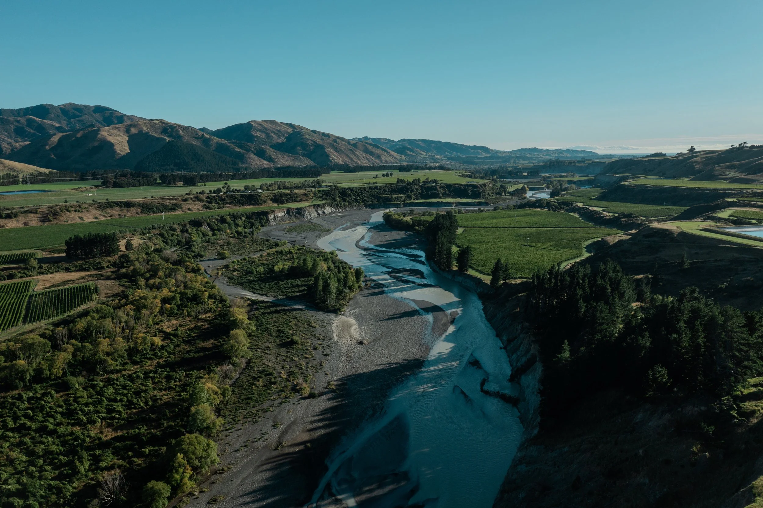 A river running through a lush green valley with mountains in the background under a clear blue sky.