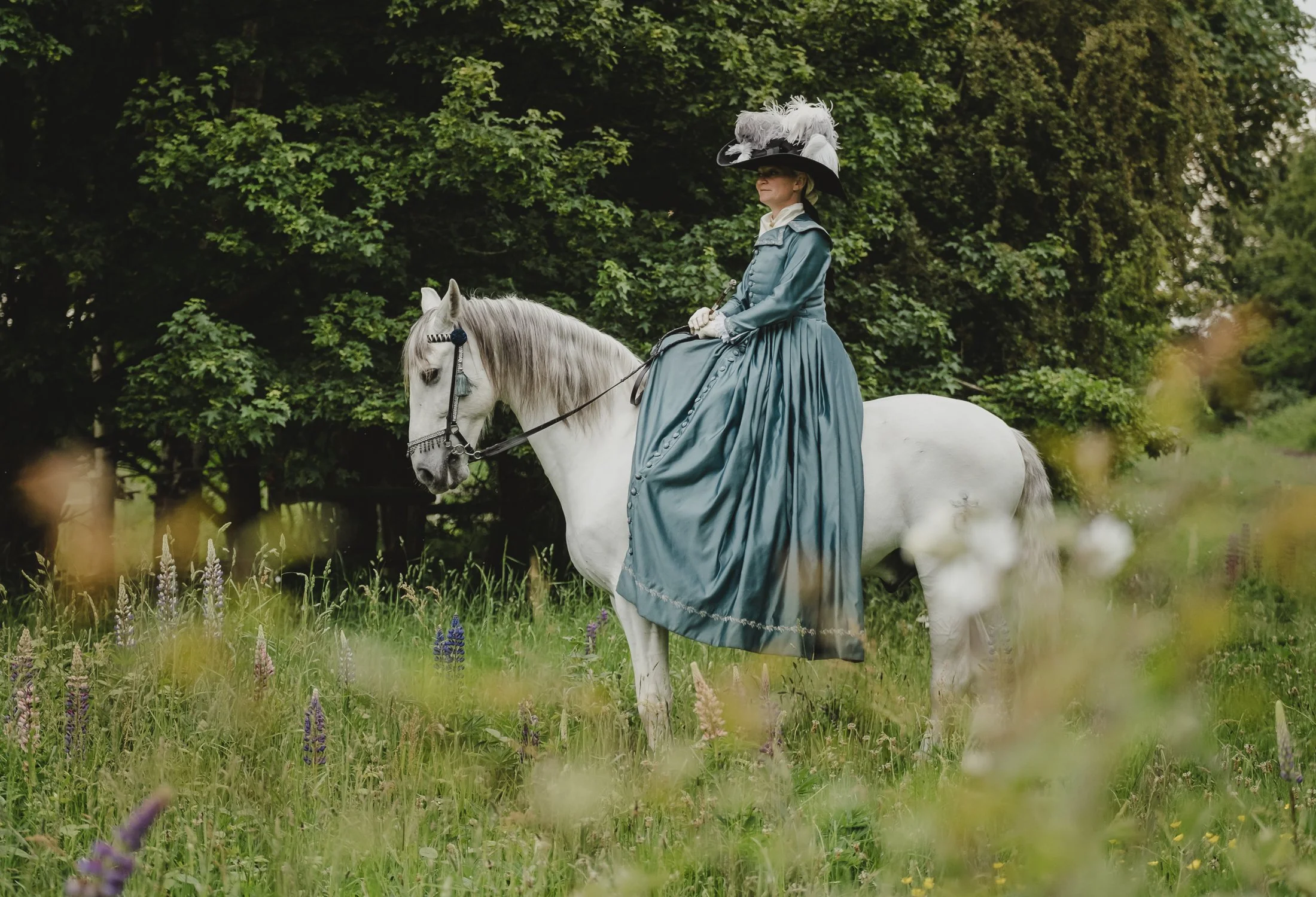 A lady dressed in a Concours D'Elegance dress riding side saddle on a Spanish Pre horse