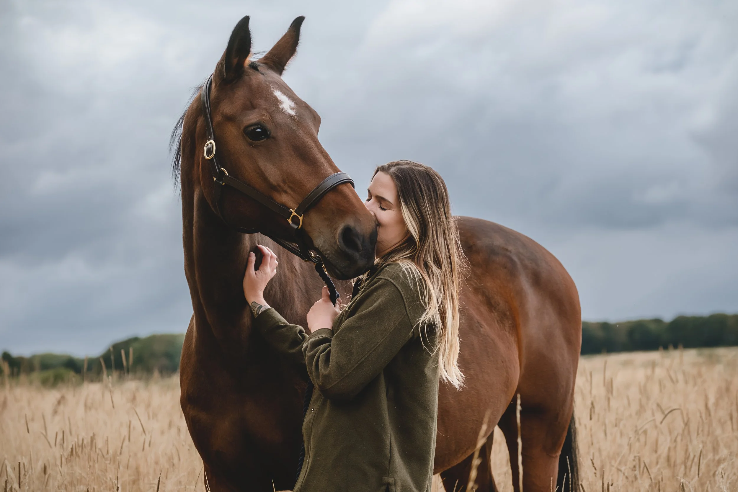 A woman hugging a brown horse in a field with overcast skies.