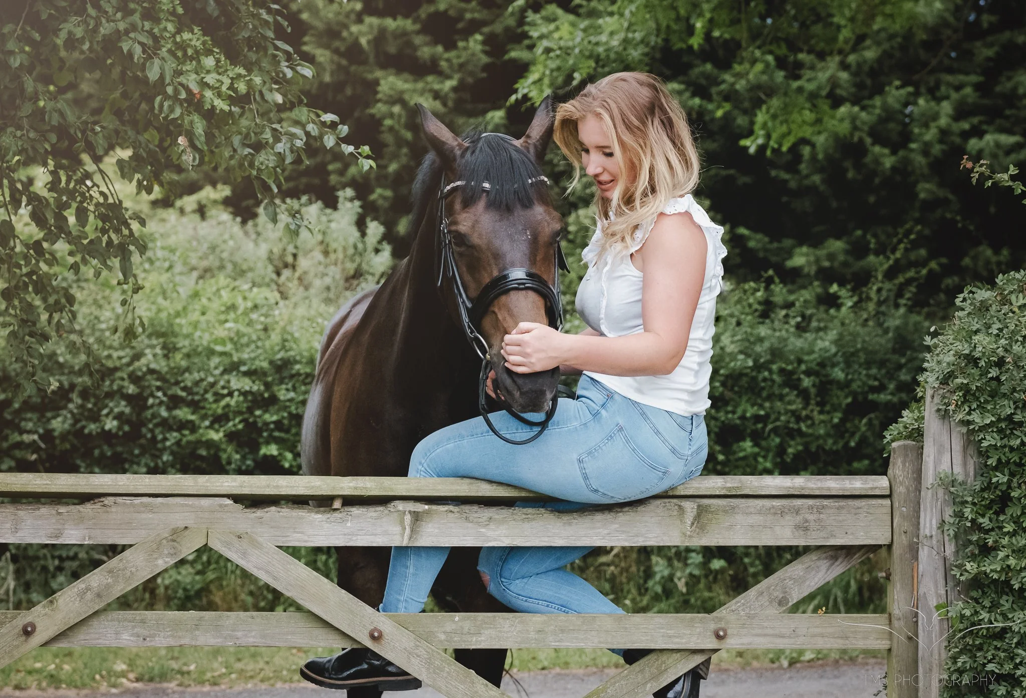Dressage rider sitting on the gate with her horse next to her