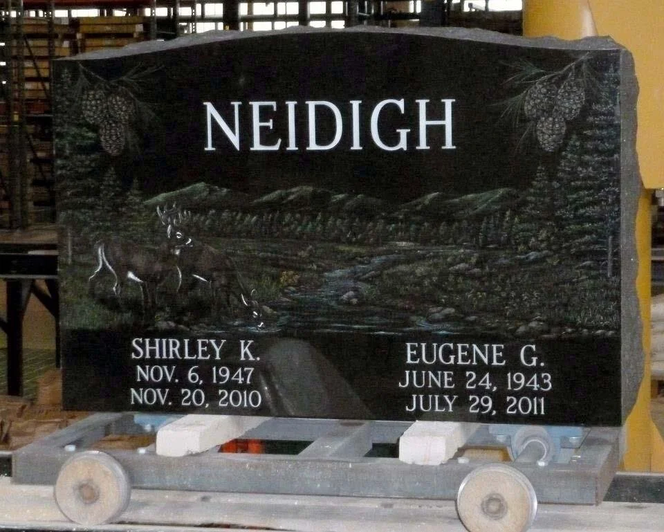 Granite cemetery headstone with "NEIDIGH" engraved at the top, featuring a nature scene with deer and trees. Below are names and dates: Shirley K. (Nov 6, 1947 – Nov 20, 2010) and Eugene G. (June 24, 1943 – July 29, 2011).