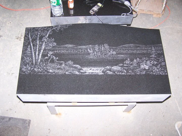 Granite slab with engraved nature scene, featuring deer in a forest landscape.