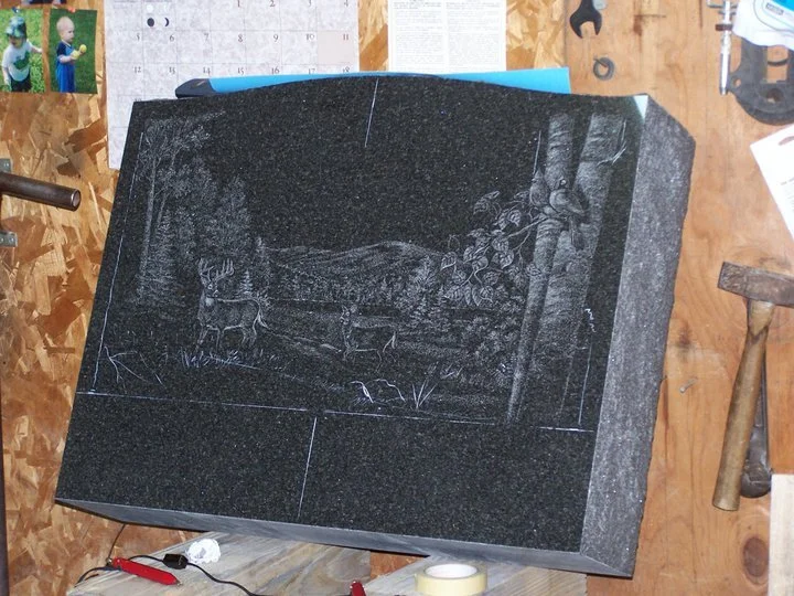 Engraved granite slab with nature scene including deer and trees in a workshop setting.