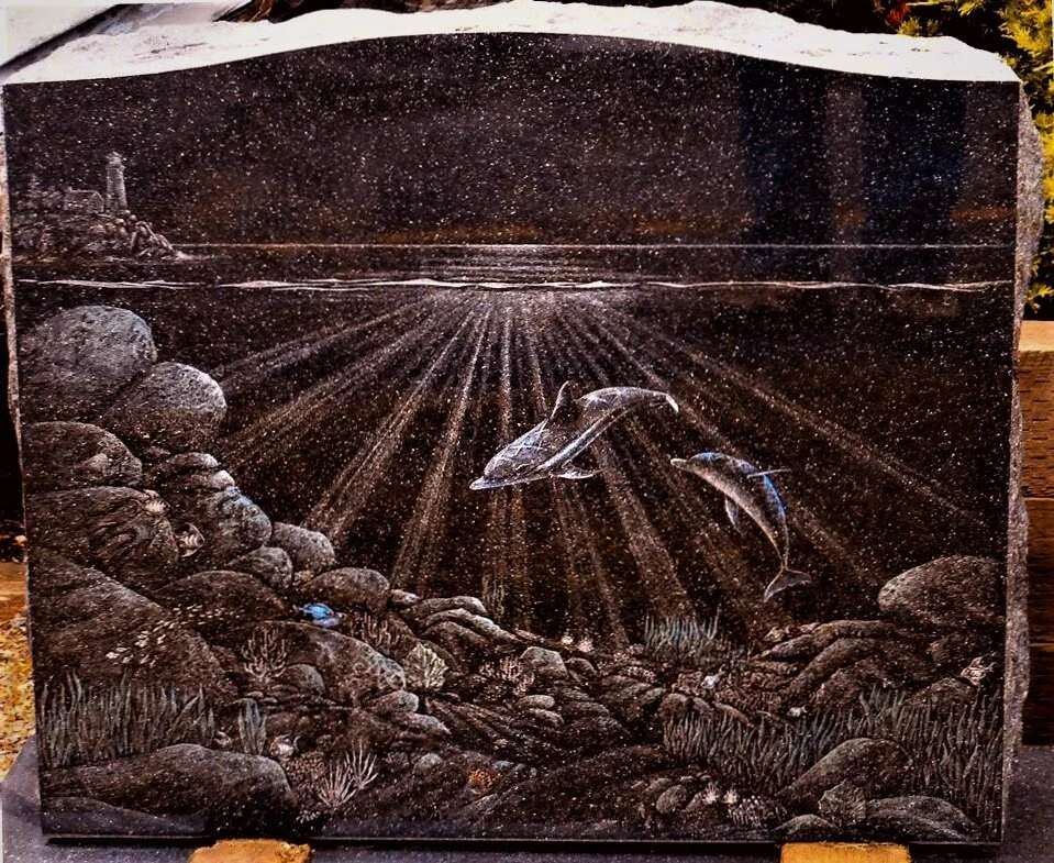 Granite etching of underwater scene with two dolphins, rocks, coral, and sun rays filtered through water, lighthouse in background.