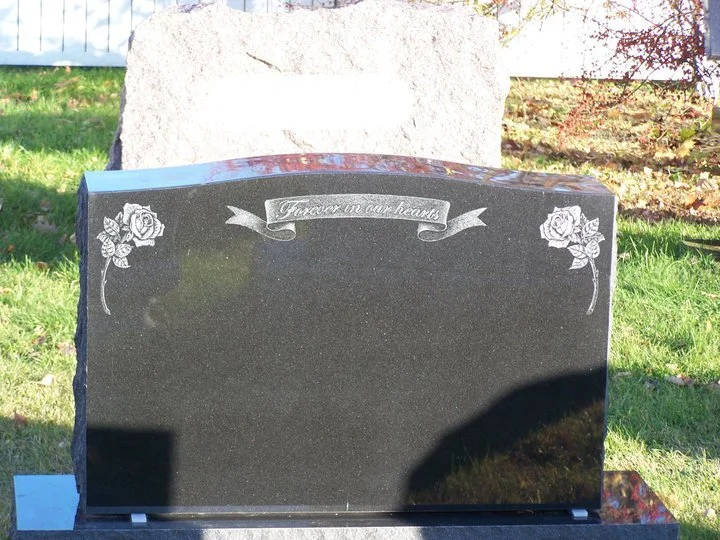 Black granite headstone with 'Forever in our hearts' inscription, surrounded by engraved roses, set in a grassy cemetery.