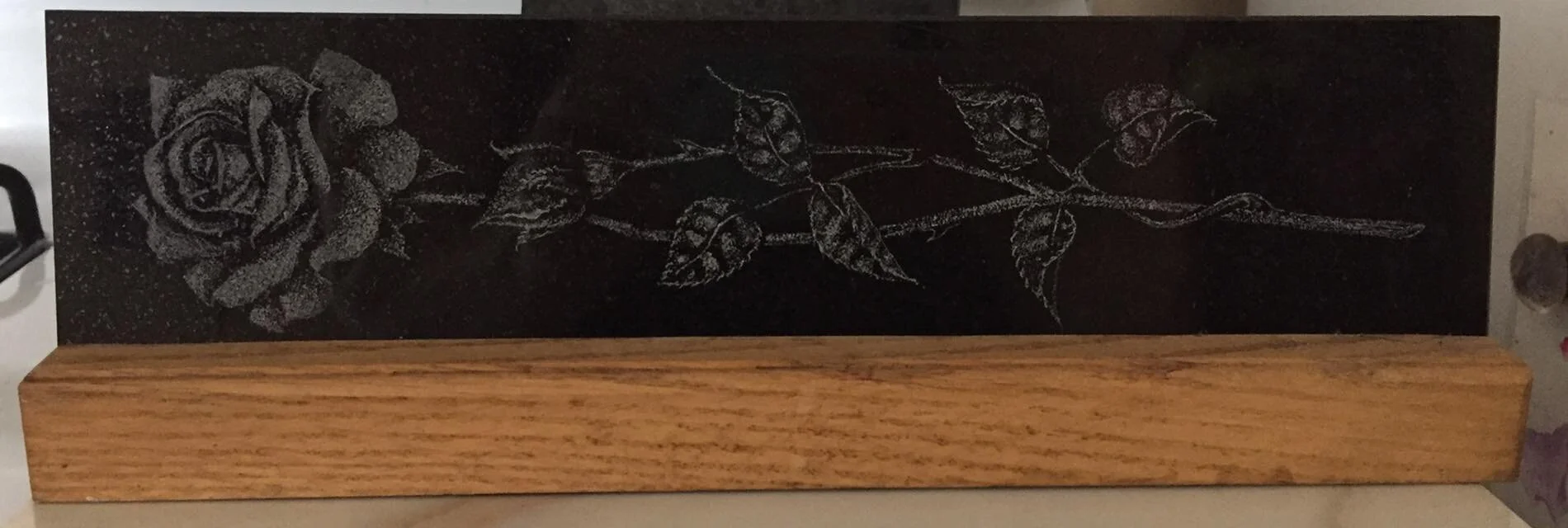 Engraved rose design on black stone with wooden base