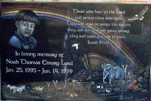 Memorial plaque with a child's portrait, biblical quote, and Noah's Ark scene. Text reads: "In loving memory of Noah Thomas Emory Lord Jan. 25, 1995 - Jun. 14, 1999." Includes Isaiah 40:31 and depiction of animals and the Ark under a rainbow.
