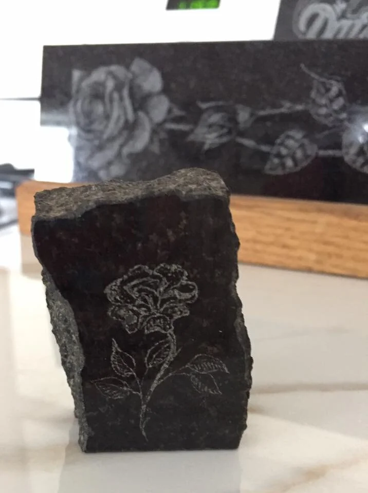 Stone with engraved floral design on front, larger engraved floral panel in background.