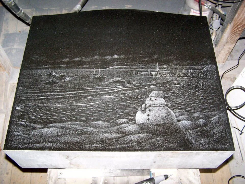 Engraved stone with snowman, seaside landscape, and boats in the background