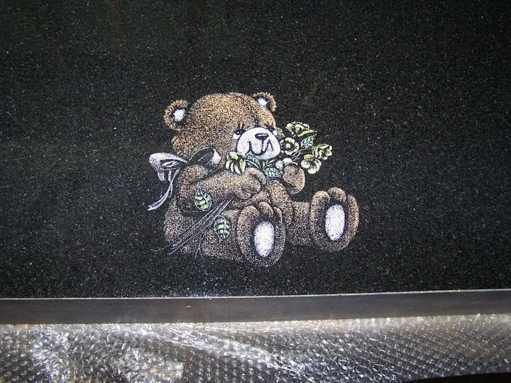 Illustration of a teddy bear holding flowers on a black granite surface.