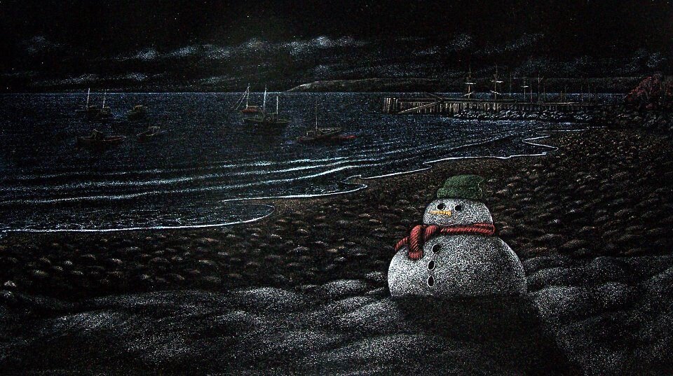 Snowman on a dark beach at night with boats in the water and a pier in the background. The sky is cloudy and the snowman is wearing a green hat and red scarf.