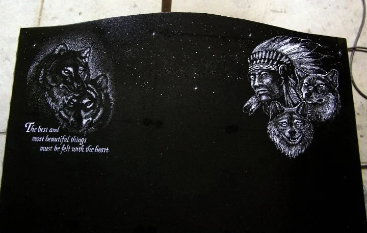 Black tombstone with white etchings of wolves and a Native American chief. Quote reads, "The best and most beautiful things must be felt with the heart."