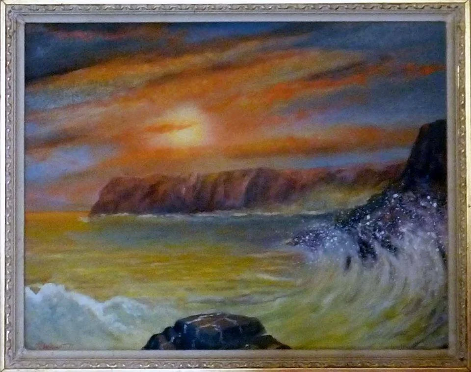 Framed painting of a coastal landscape with cliffs, ocean waves, and a colorful sunset sky.