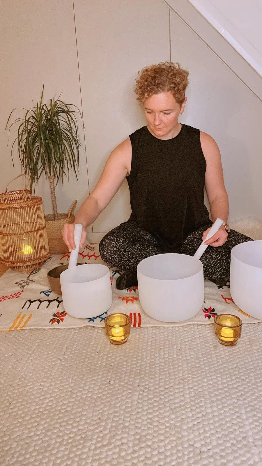 rowena sitting crossed legged playing crystal bowls in a calming quiet room with candles