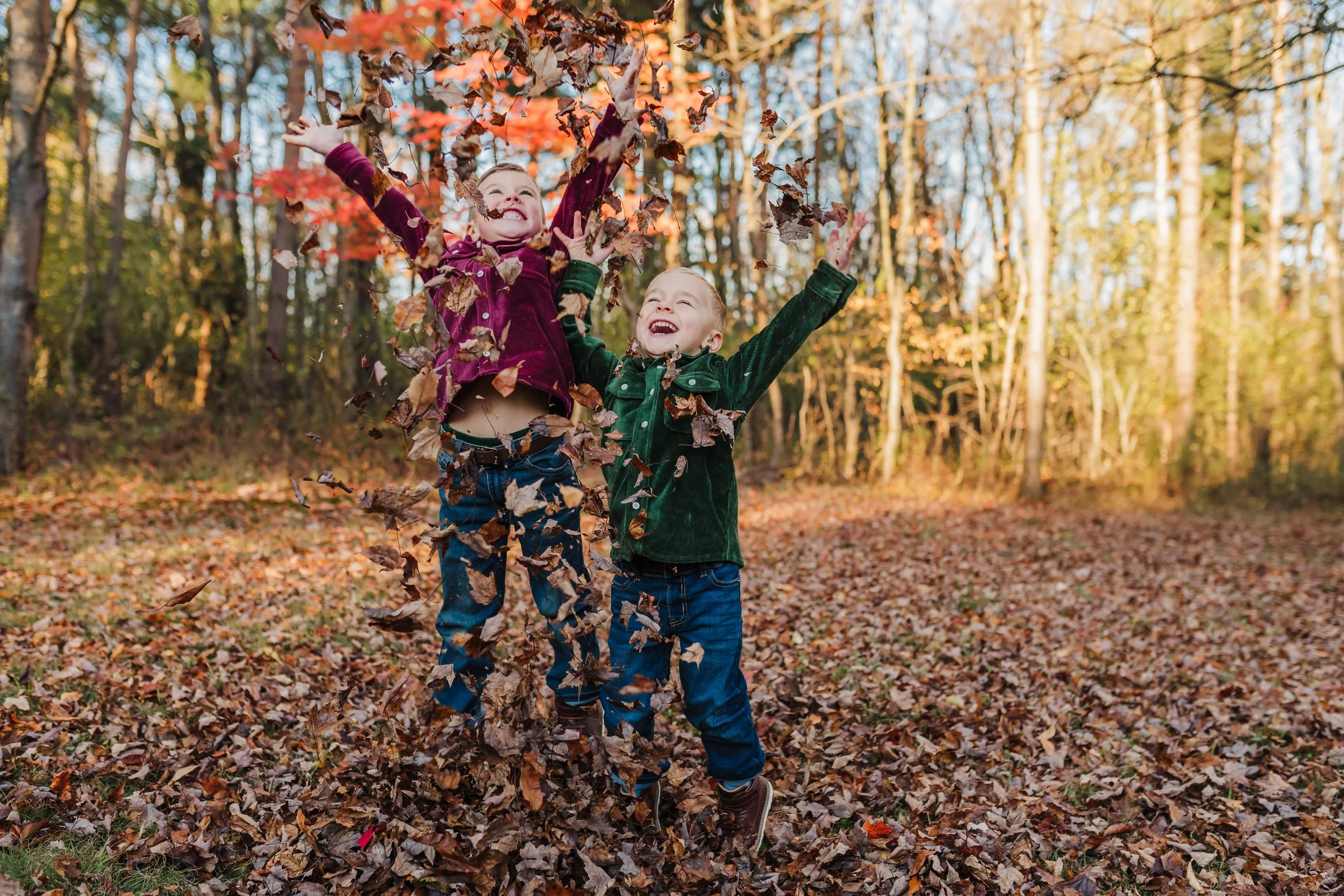 two boys throwing fall leaves in the air and laughing