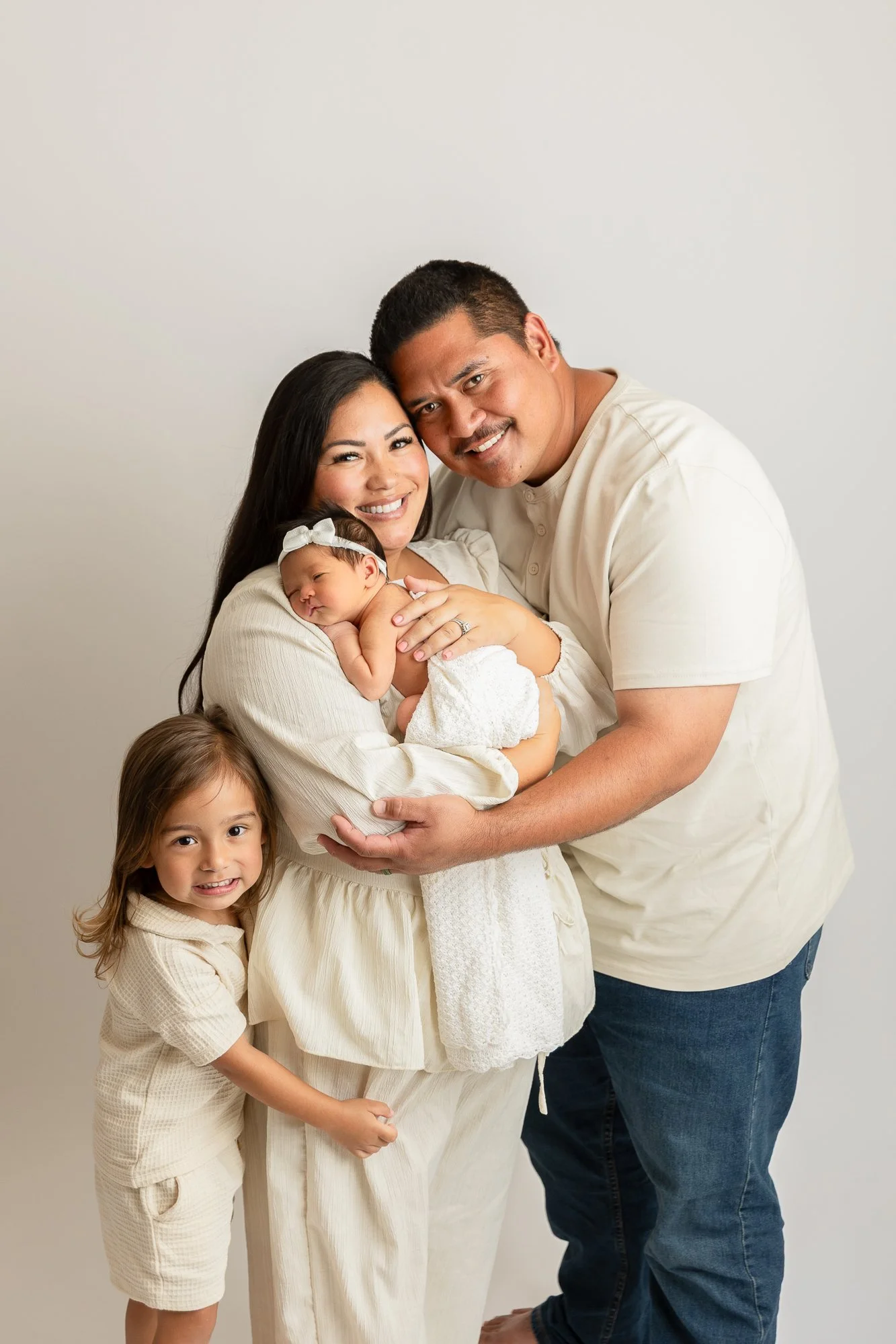 Three children sitting together; a young girl holding a swaddled baby and a boy sitting beside them, all smiling.