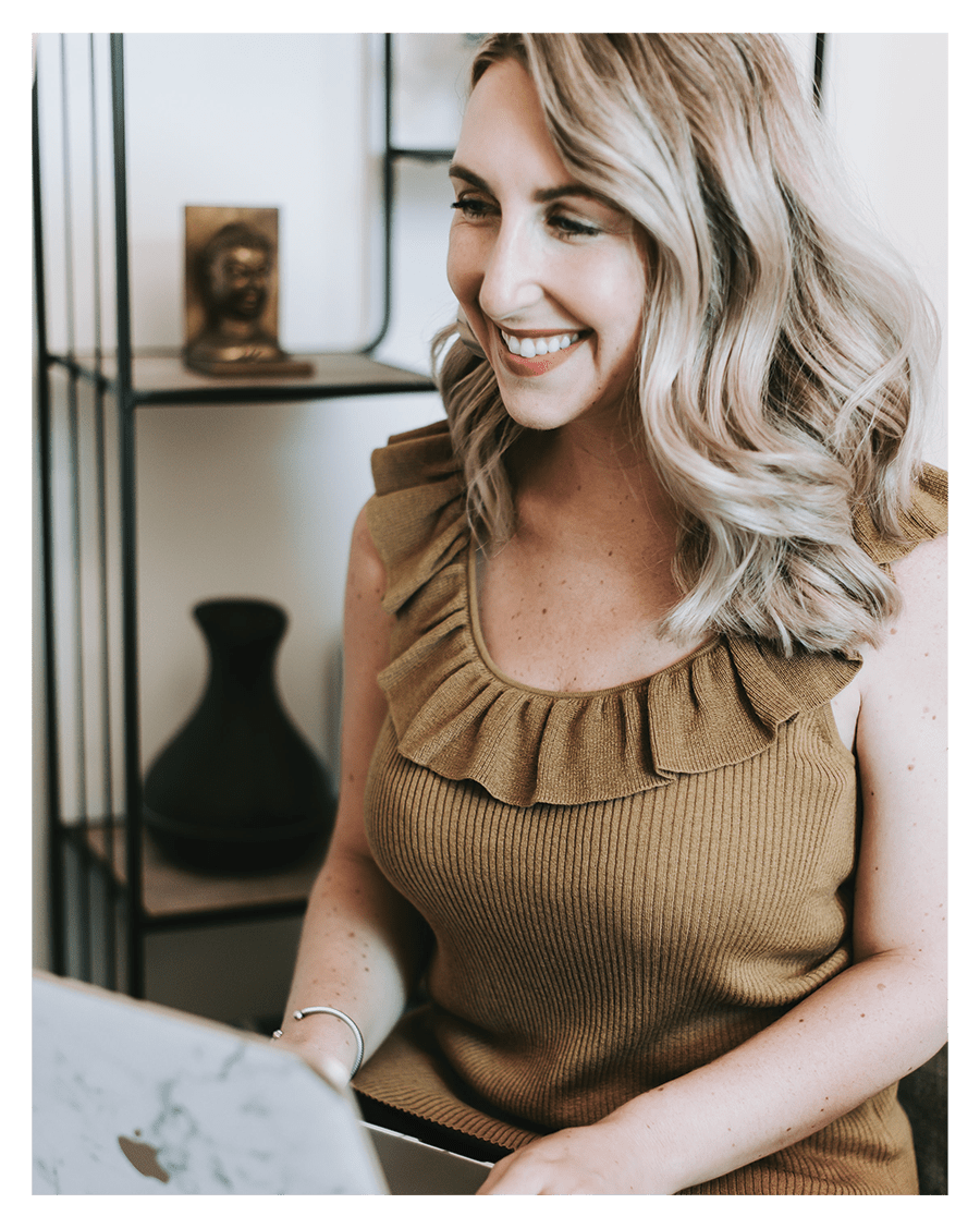 A smiling woman with wavy blonde hair working on a laptop in a cozy home office.