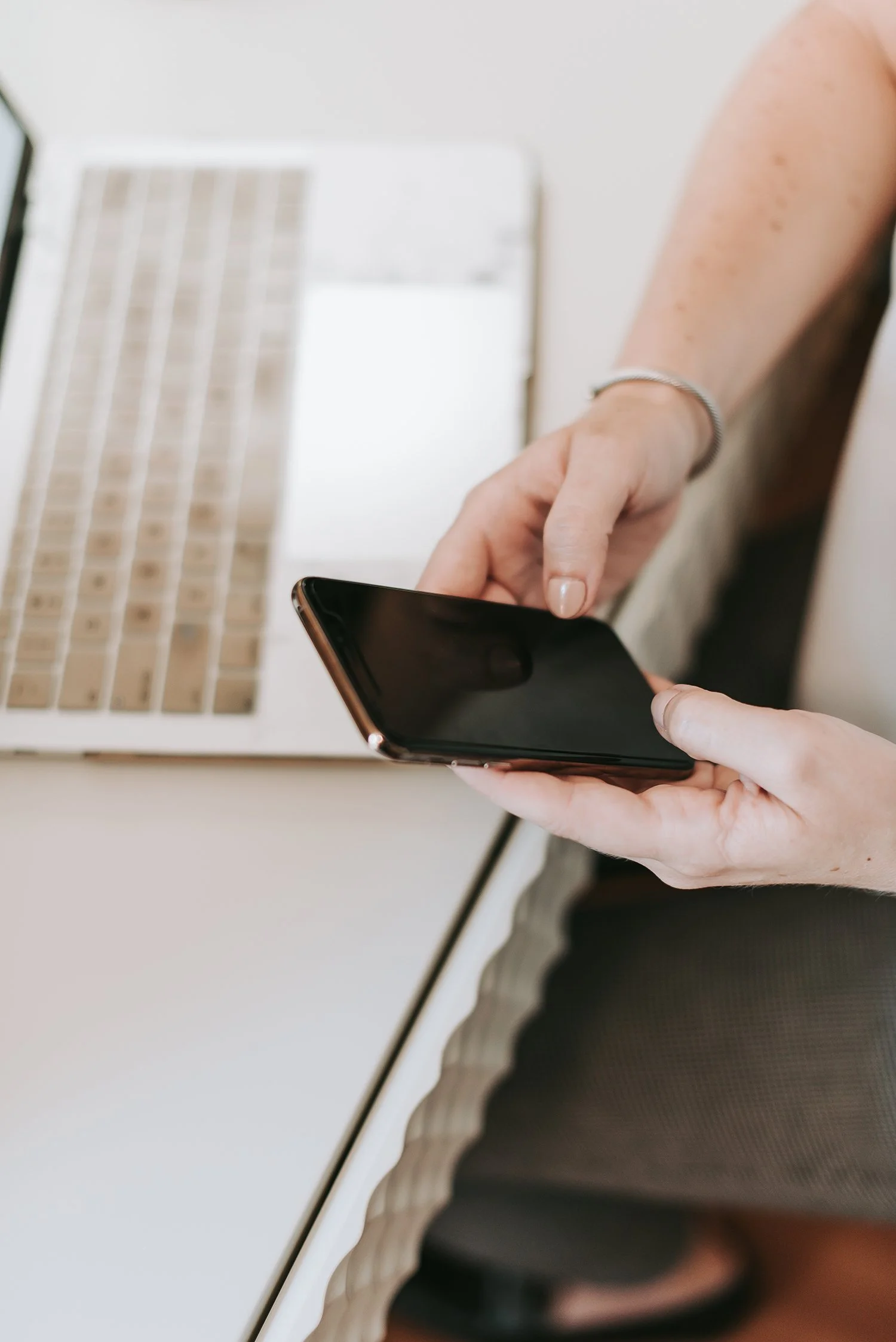 Person using a smartphone with a laptop in the background.
