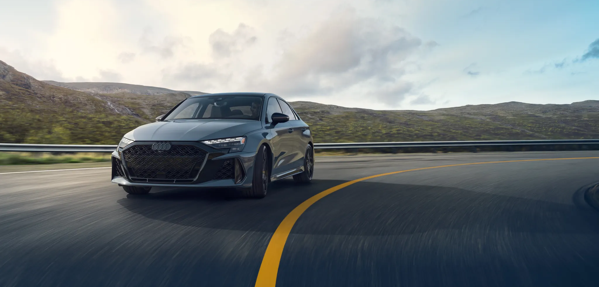 Black Audi car on an empty mountain road with forest and mountains in the background.