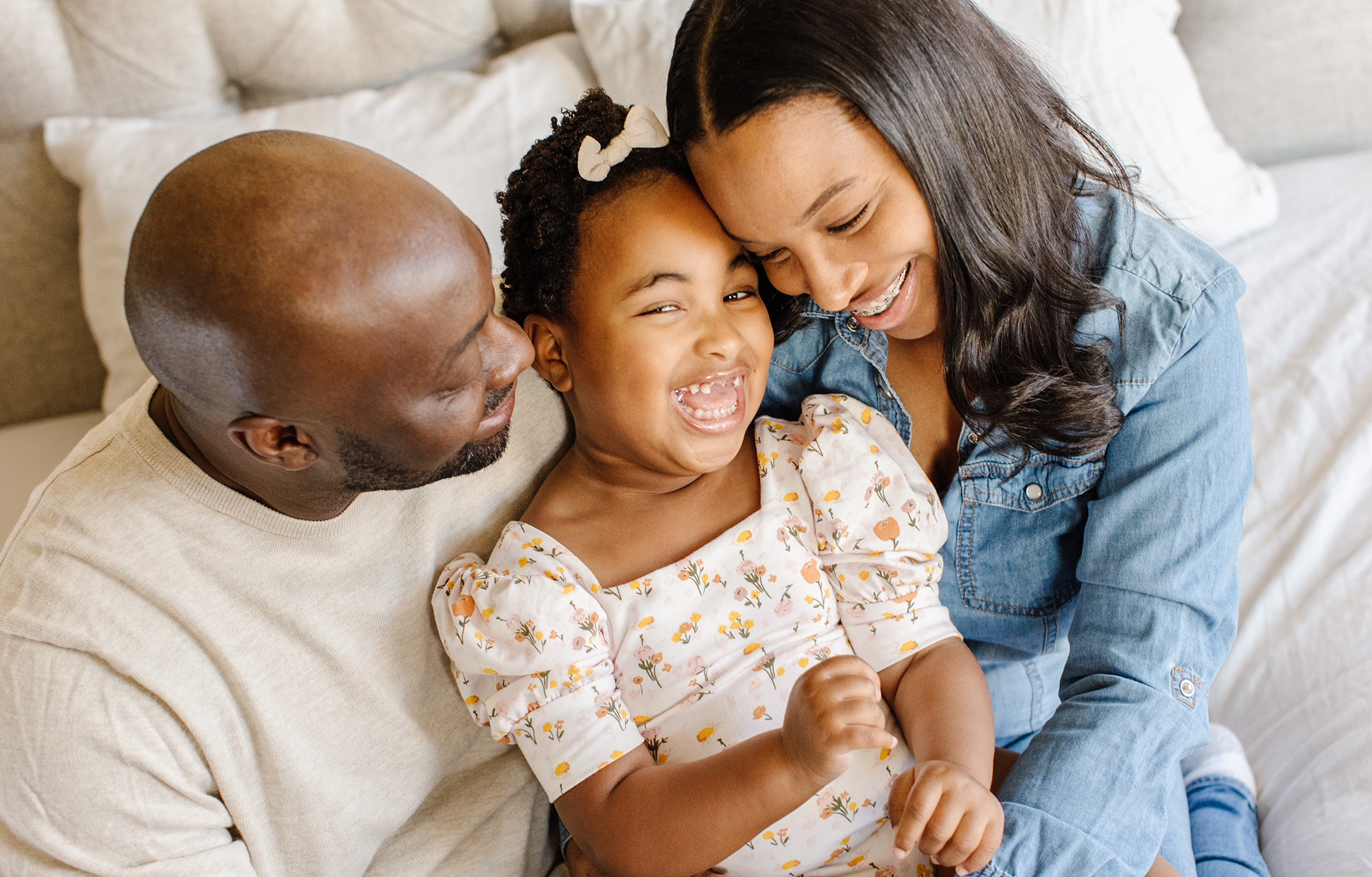 A happy family sitting on a bed: father, mother, and daughter sharing a joyful moment