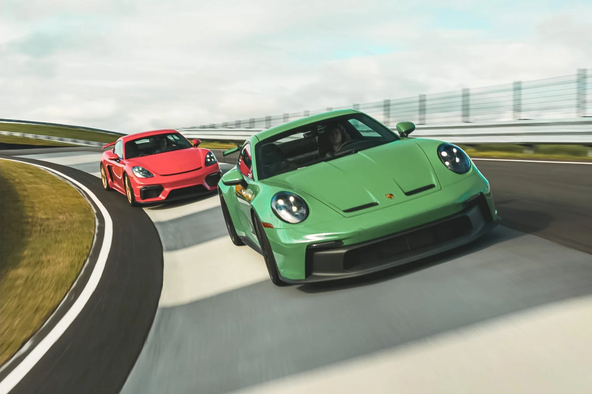 Two sports cars, a green one and a red one, racing on a curved track under a partly cloudy sky.