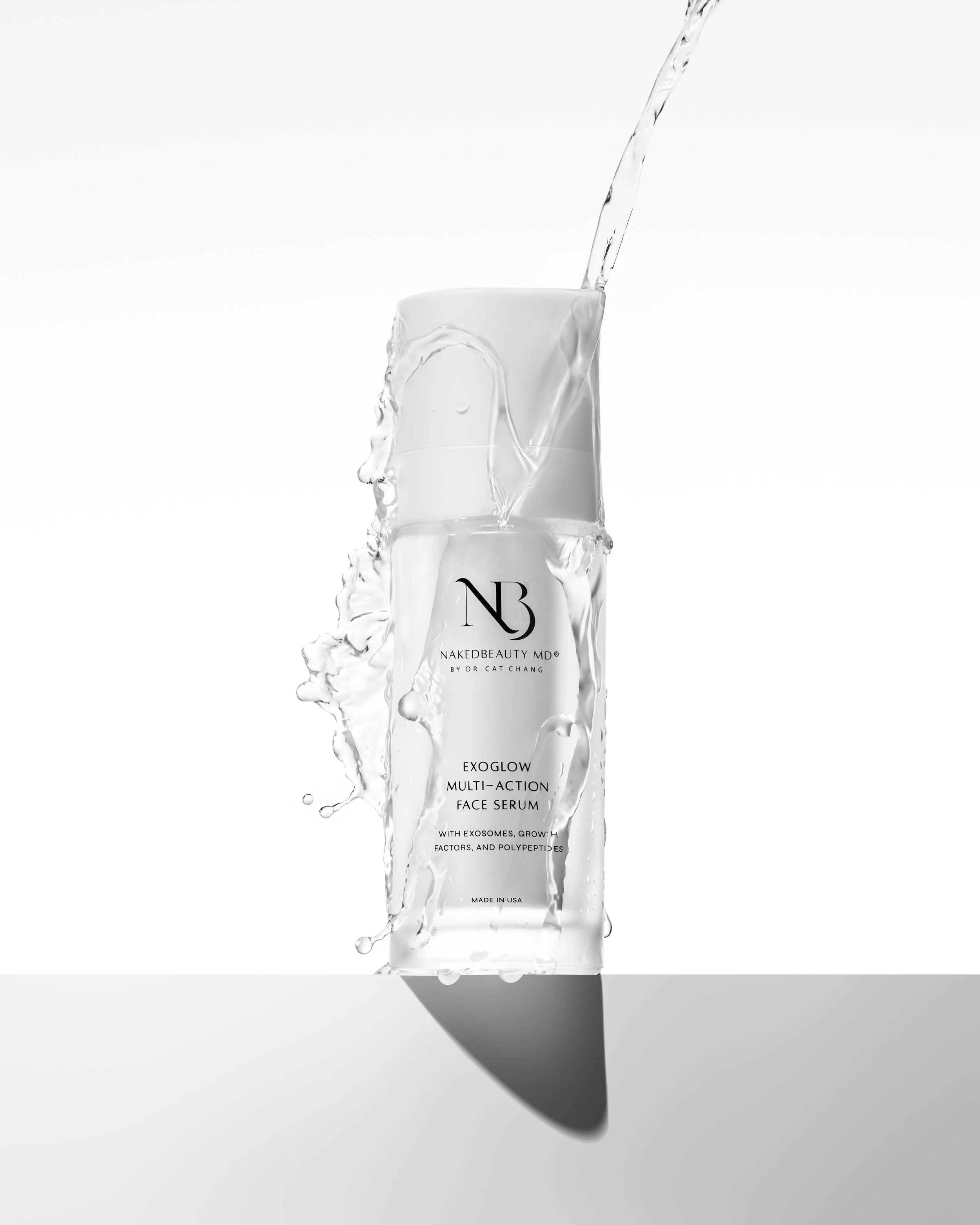 Bottle of Naked Beauty MD ExoGlow Multi-Action Face Serum with water splashing around it, set against a white background.