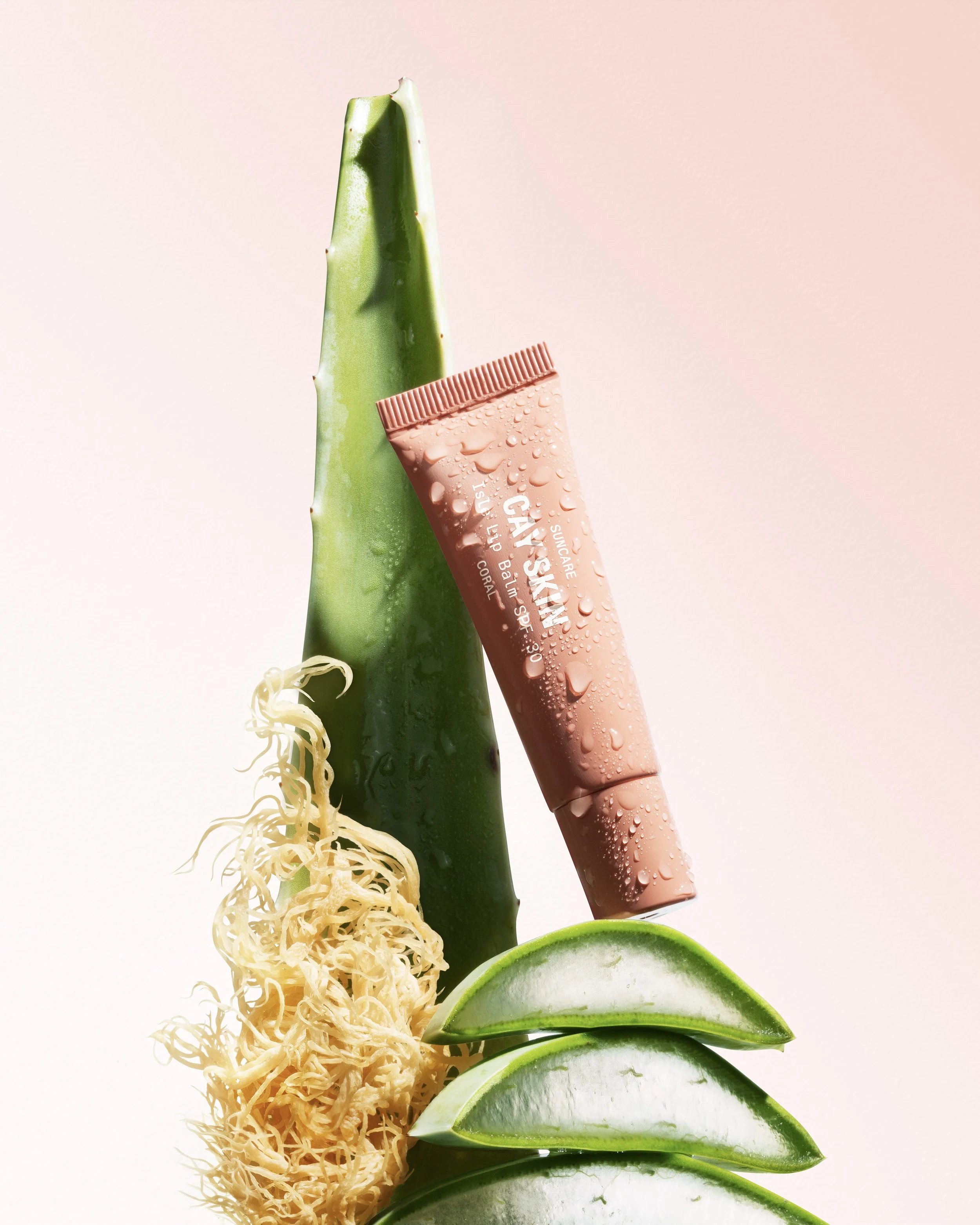 Aloe vera leaf, three lime wedges, aloe vera gel, and a bottle of sunscreen lotion with drops on the surface.