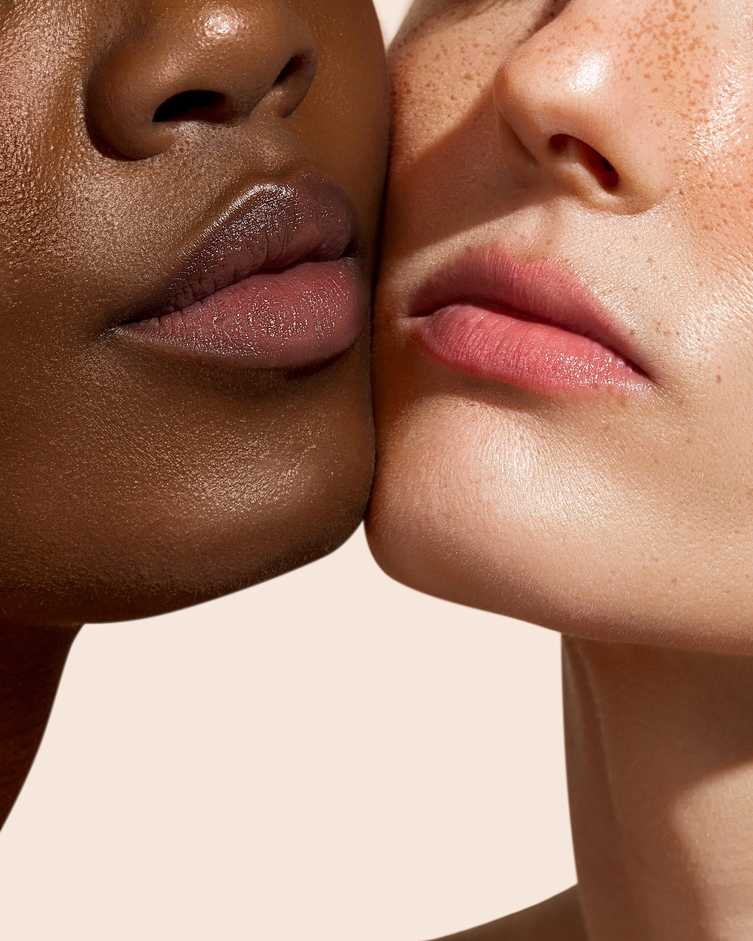 Close-up of two people's faces pressed closely together, showing their lips and noses. One person has dark skin and the other has light skin.