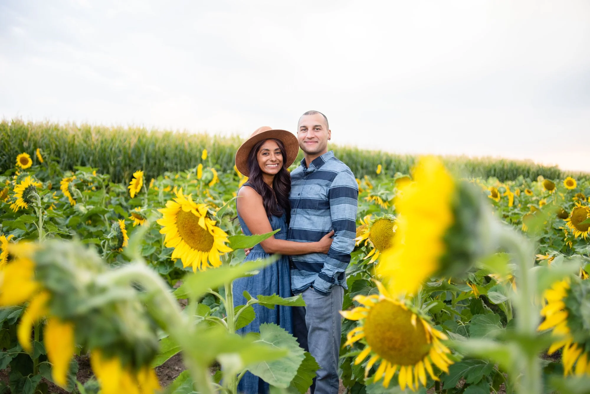 A smiling couple embracing in a sunflower field, with a cloudy sky overhead. Declo sunflower photos, Southeastern Idaho Photographer, Engagement Photos