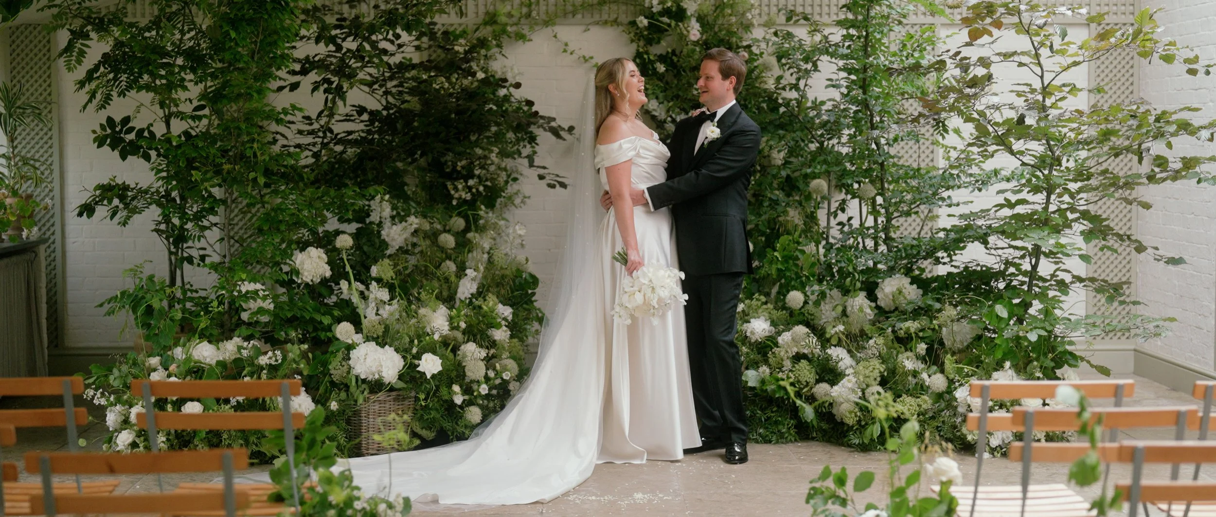 Kin House bride and groom standing in front of lush green and white florals.